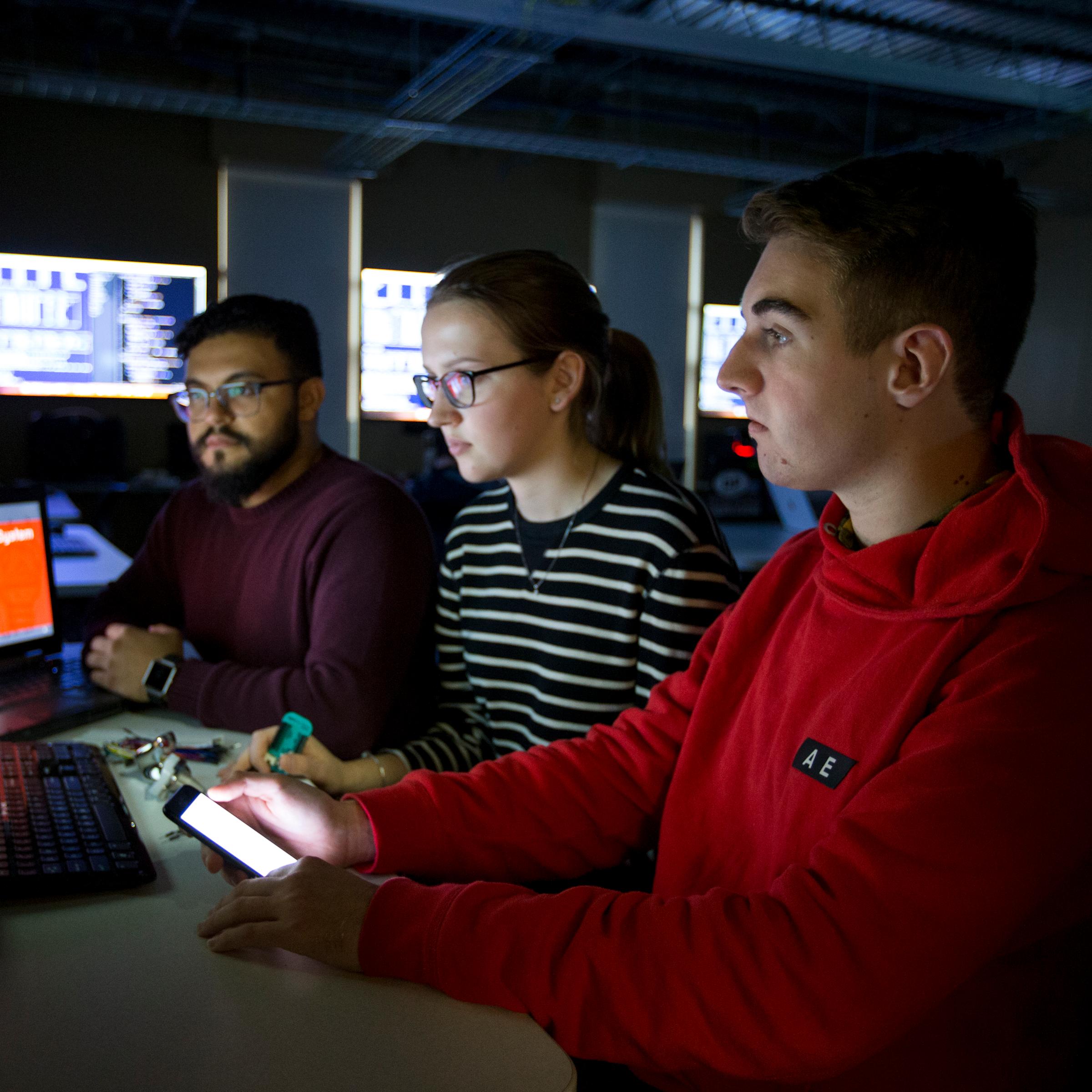Three students looking at a laptop in dark room
