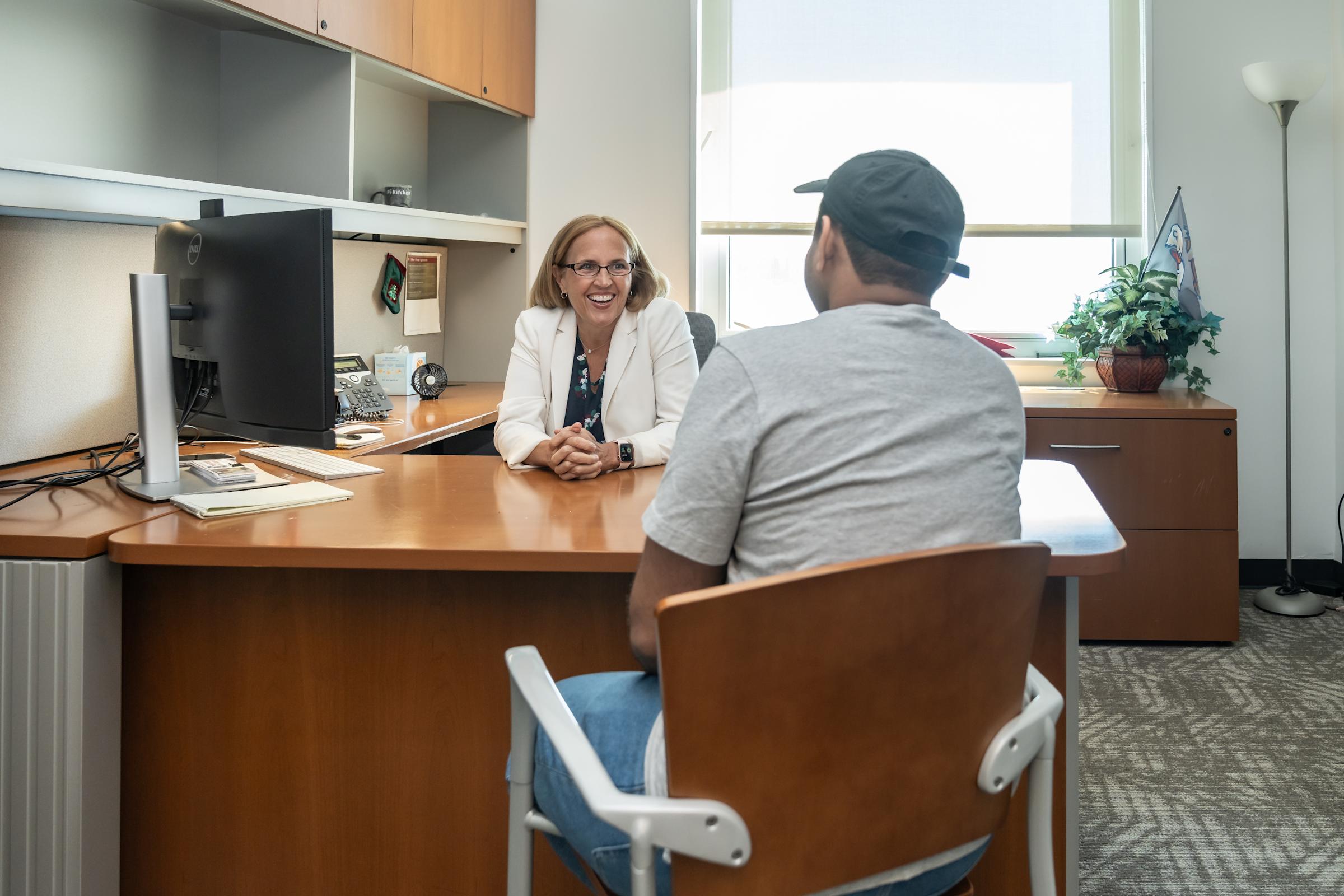 Michelle Crilly sits behind her desk chatting with a student.