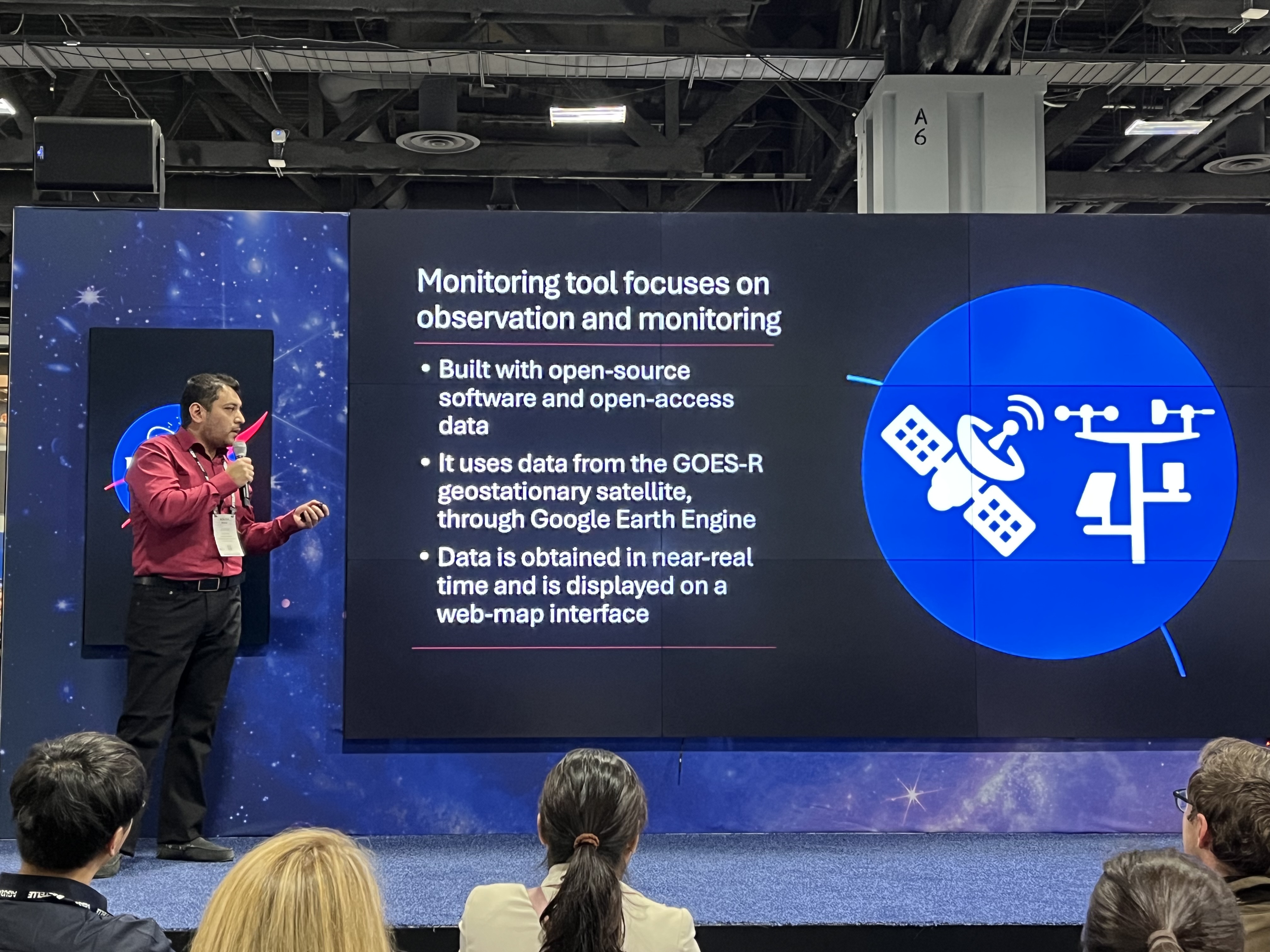 Jorge Bravo, a Stevens Ph.D. student, standing on stage presenting to an audience a slide about weather observation and monitoring.