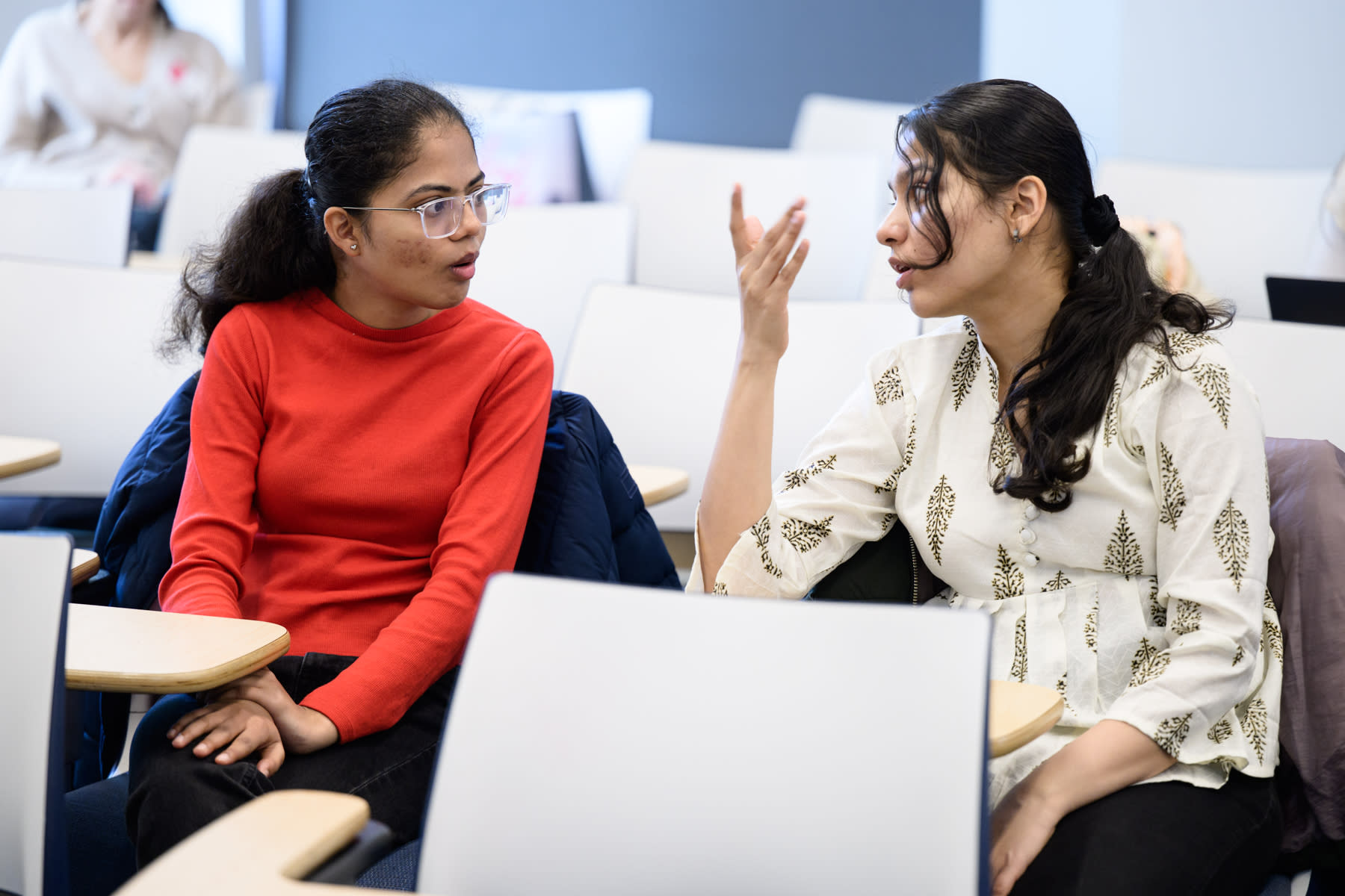 Two women, sitting in desk chairs, having a conversation. 