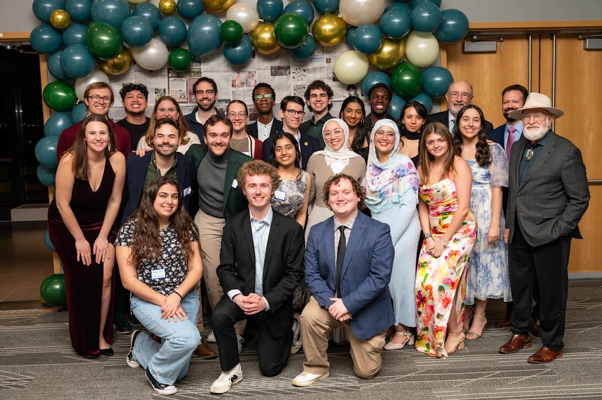 Students, alumni and guests pose for a group photo at an indoor gala event near balloon arch.