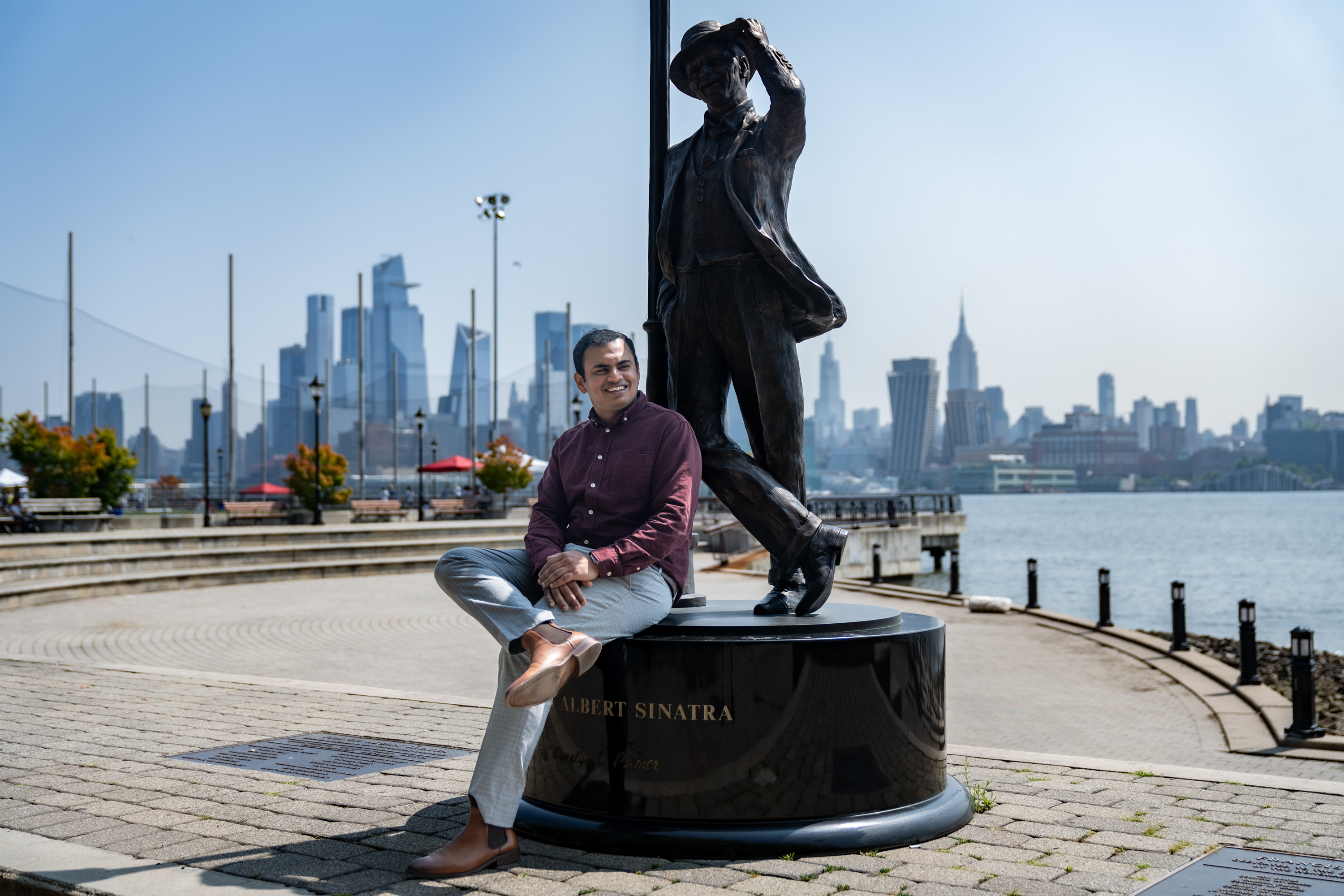Mani sits on the Frank Sinatra statue in Hoboken with part of the New York City skyline behind him. 