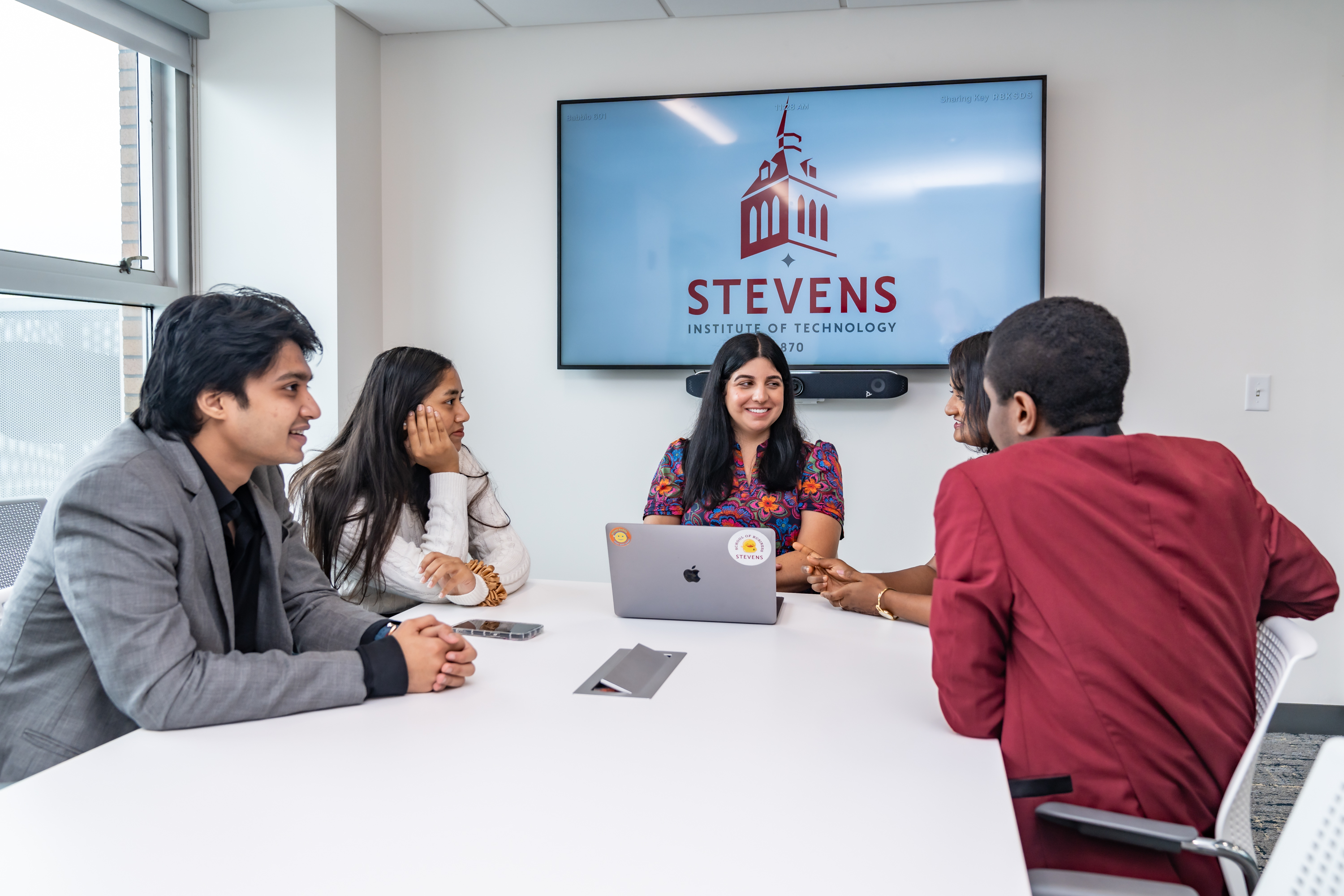 Christina Allele, Program Manager of the  Industry Capstone Program, sits down and works with a group of MBA students at a white table. 