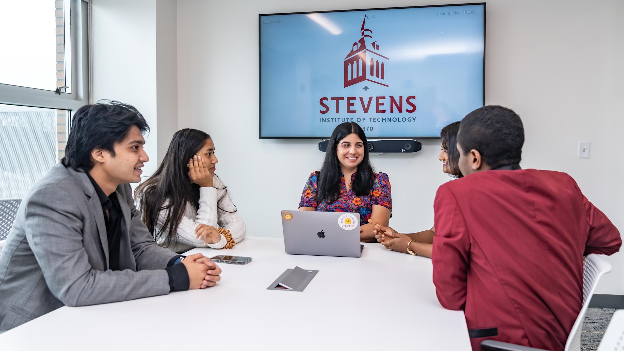 Christina Allele, Program Manager of the Industry Capstone Program, sits down and works with a group of MBA students at a white table.