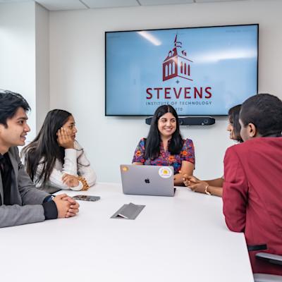 Christina Allele, Program Manager of the Industry Capstone Program, sits down and works with a group of MBA students at a white table.