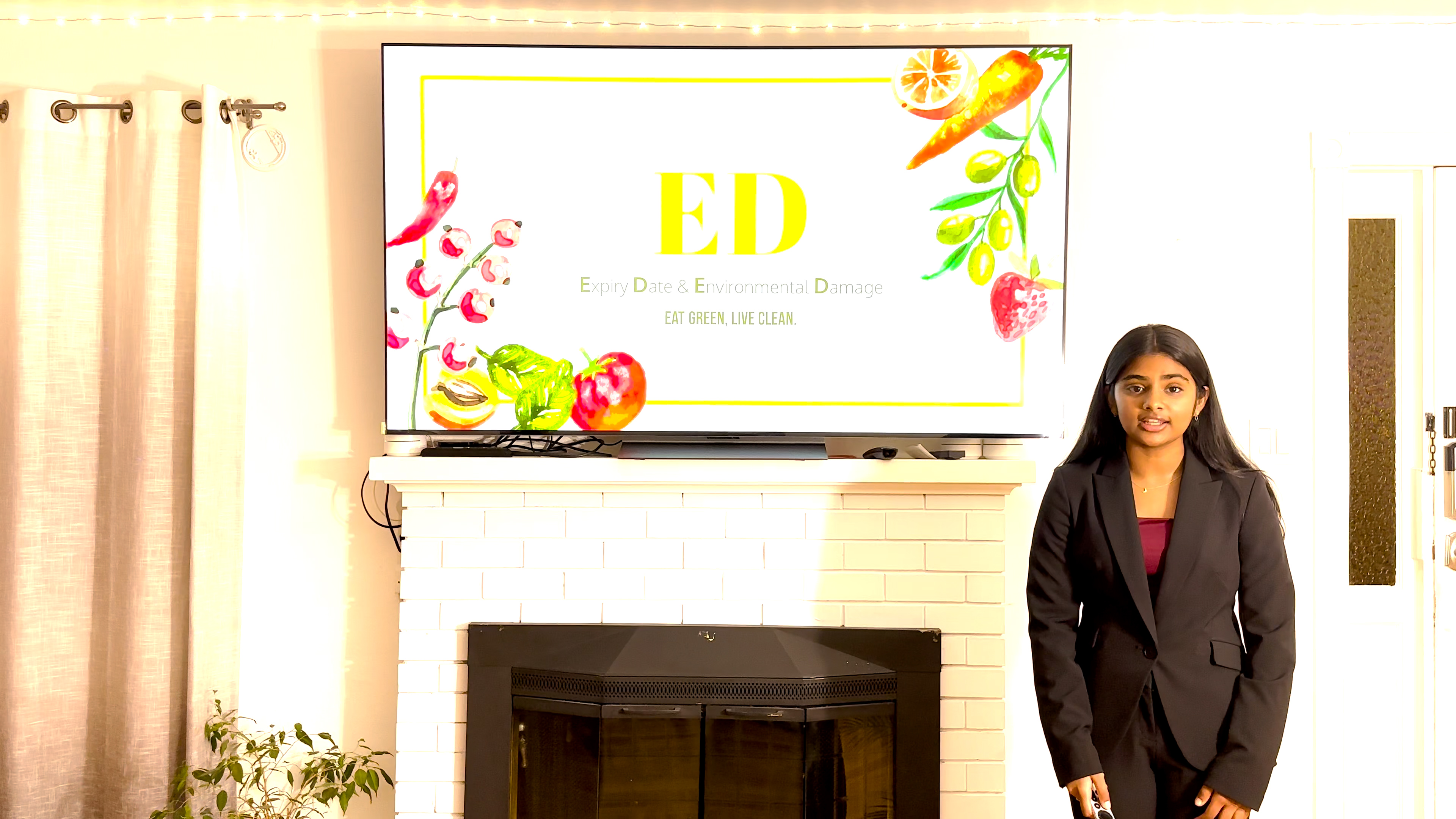 Girl in black business suit stands in front of a television screen displaying the name of the project, ED. 
