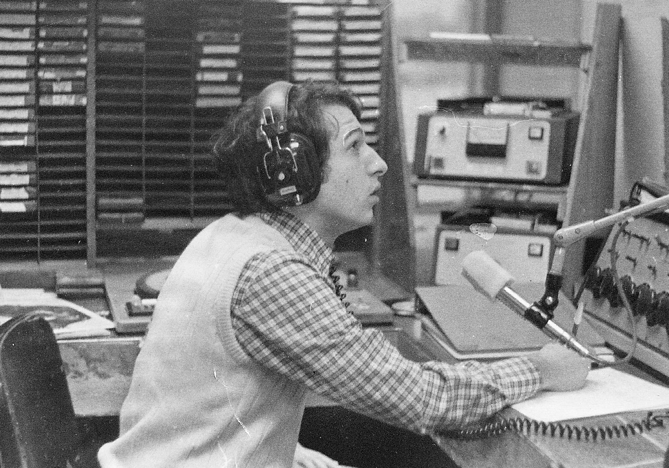 Black and white photo featuring Paul Porzio ’77 speaking into a radio microphone while seated and wearing headphones at WCPR at Stevens in 1975