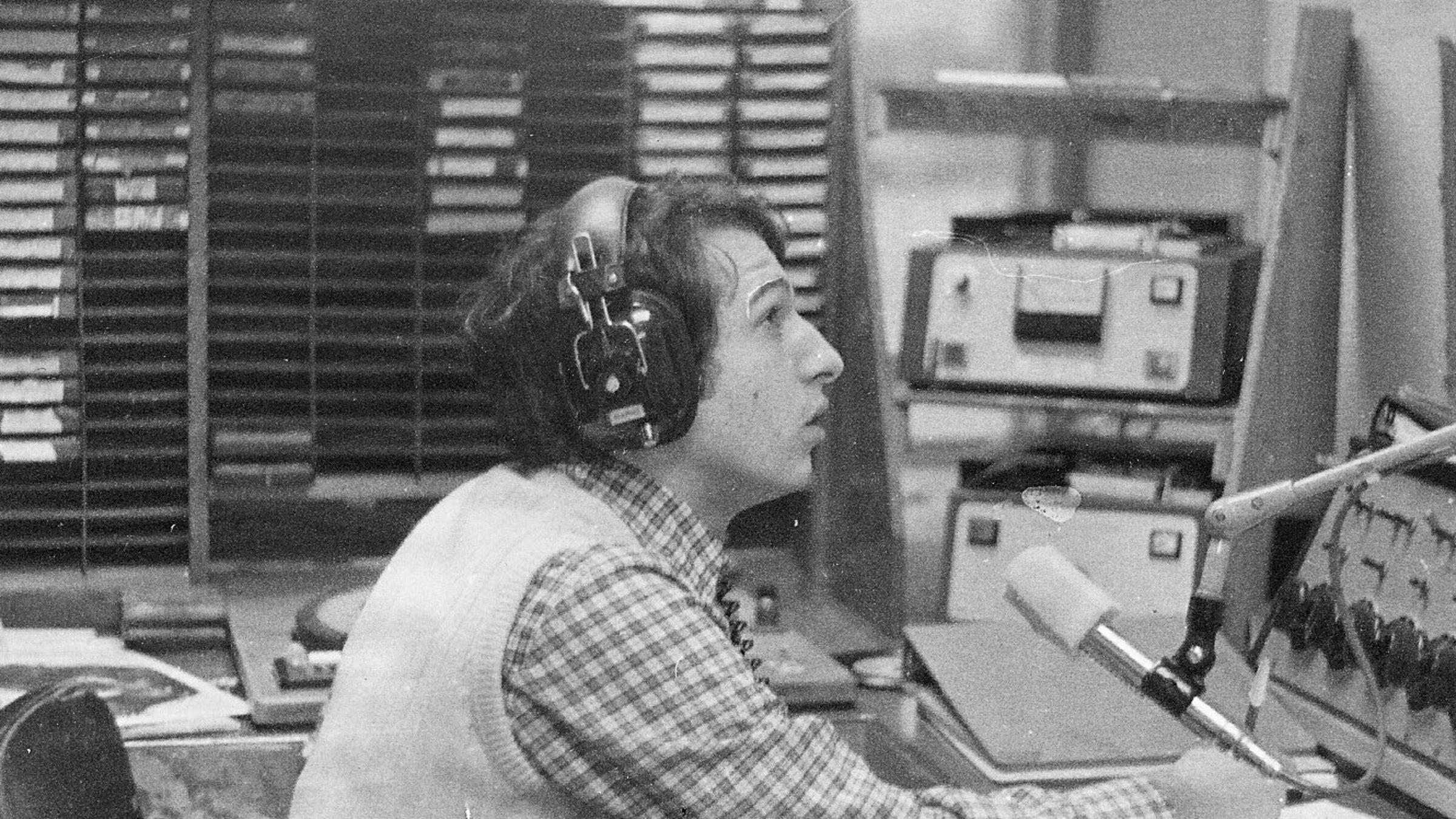 Black and white photo featuring Paul Porzio ’77 speaking into a radio microphone while seated and wearing headphones at WCPR at Stevens in 1975