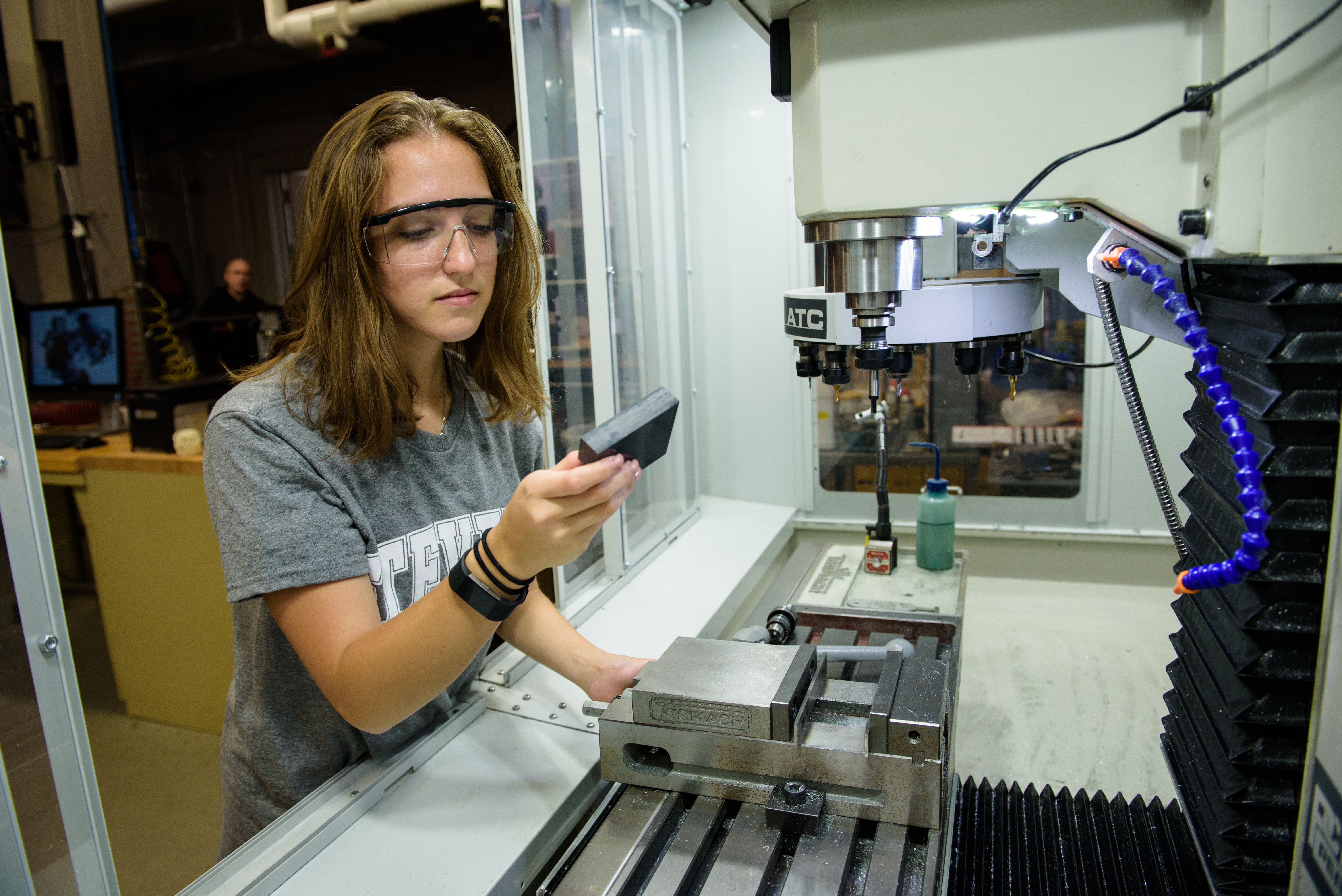 Three students examine work inside of a lab in front of a large window,