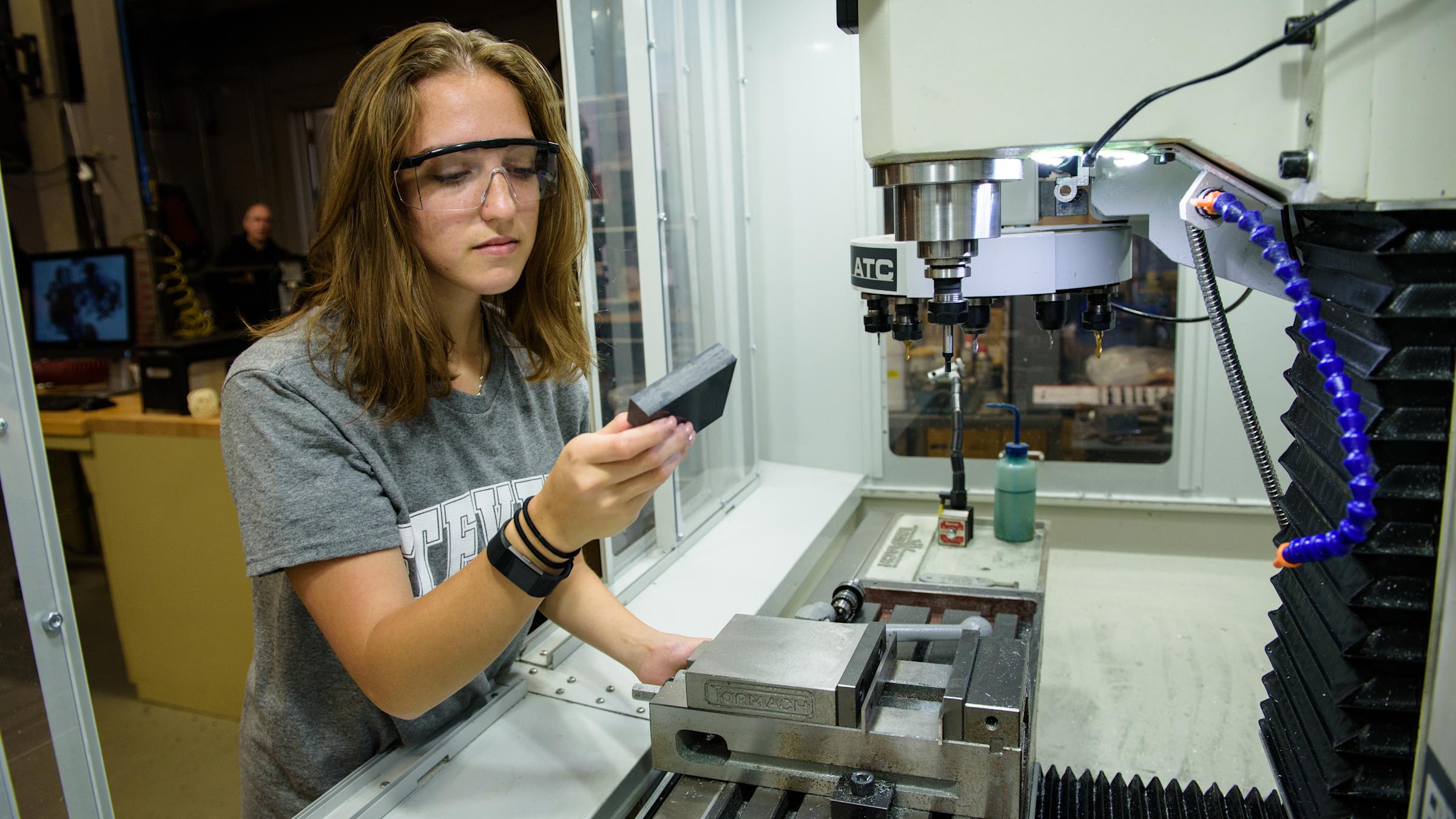 Three students examine work inside of a lab in front of a large window,