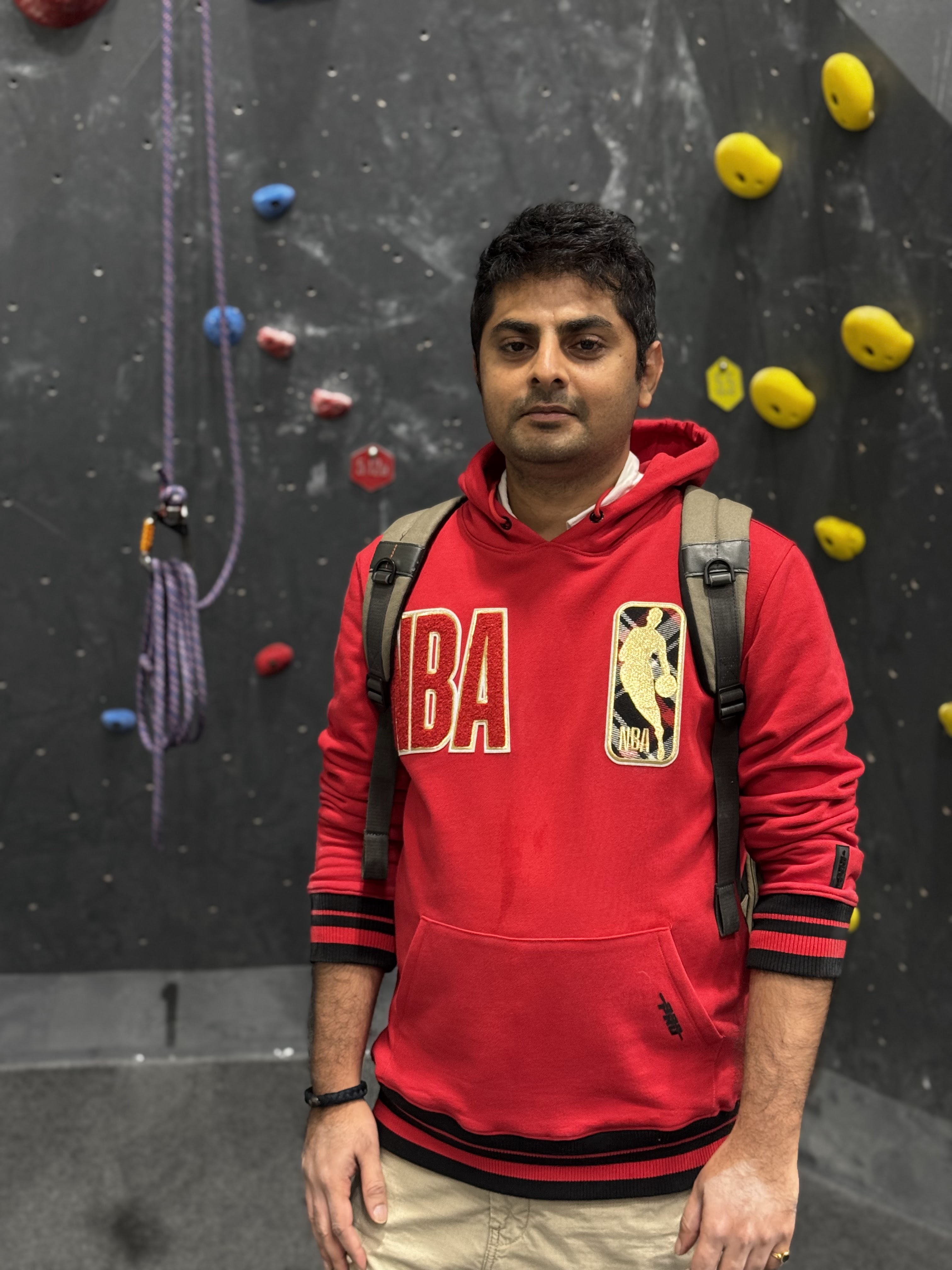 Devesh Bhosale in front of a rock-climbing wall, wearing a red NBA sweatshirt