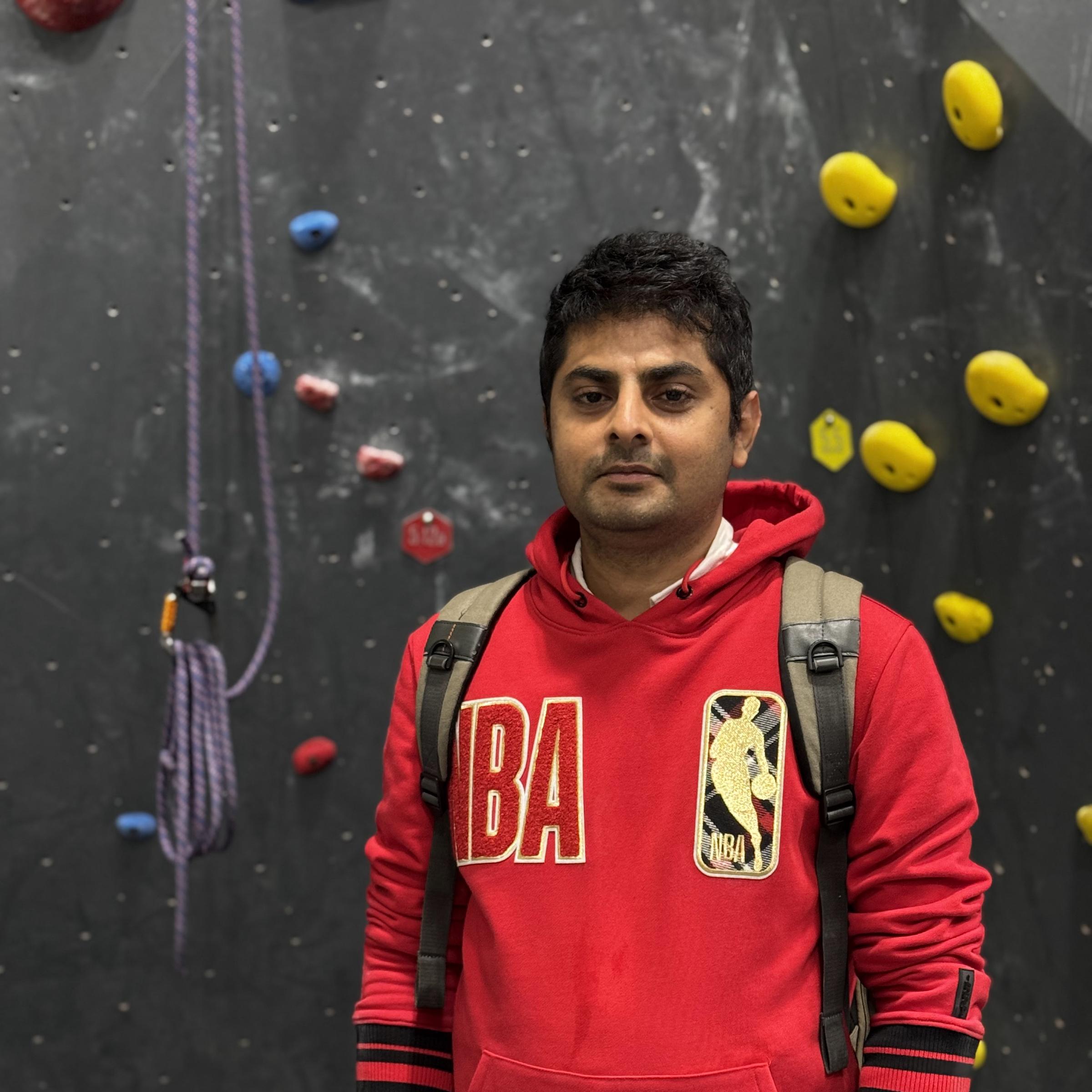 Devesh Bhosale in front of a rock-climbing wall, wearing a red NBA sweatshirt