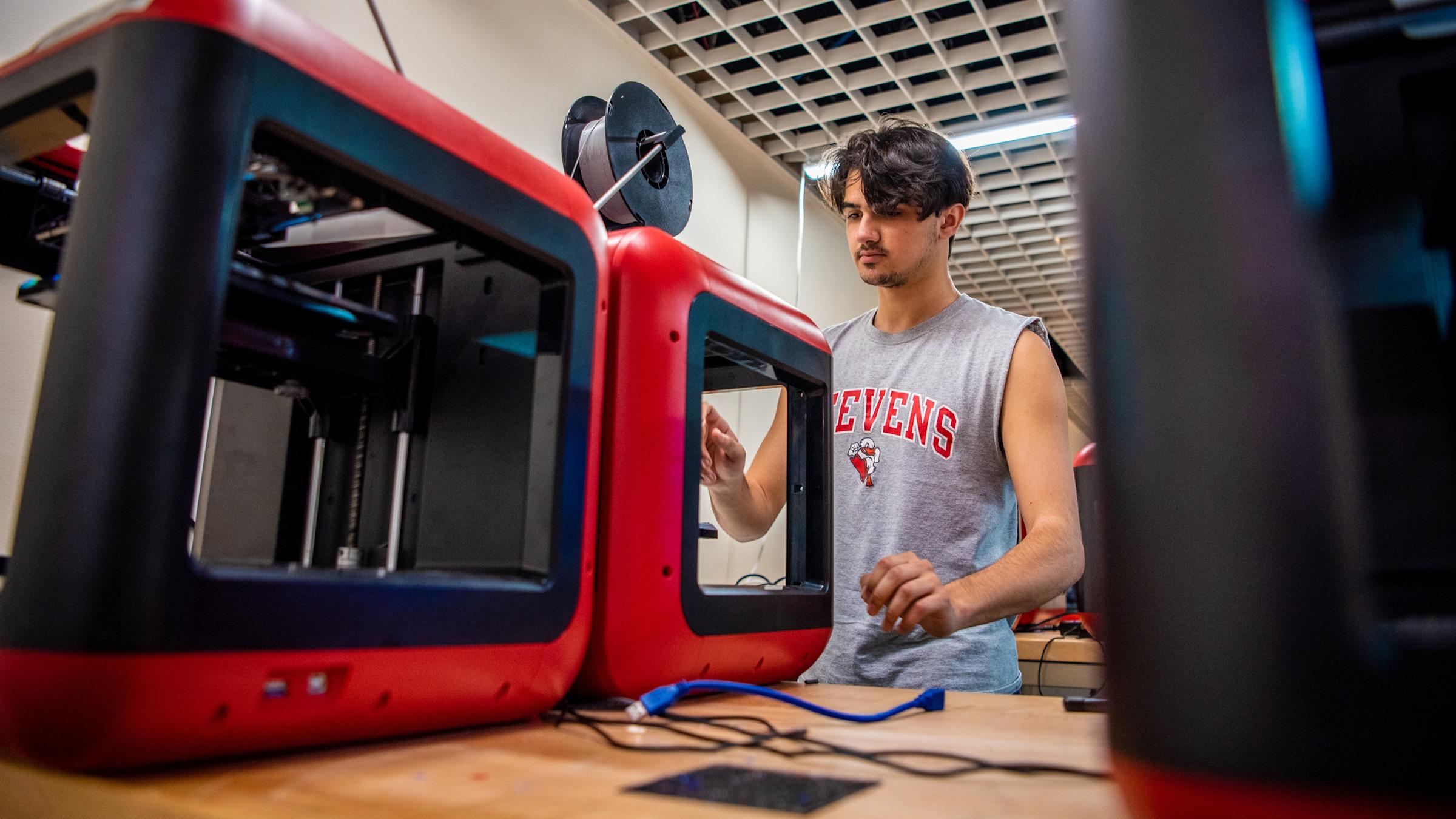 A male student in a Stevens muscle t-shirt works with equipment in a robotics lab.