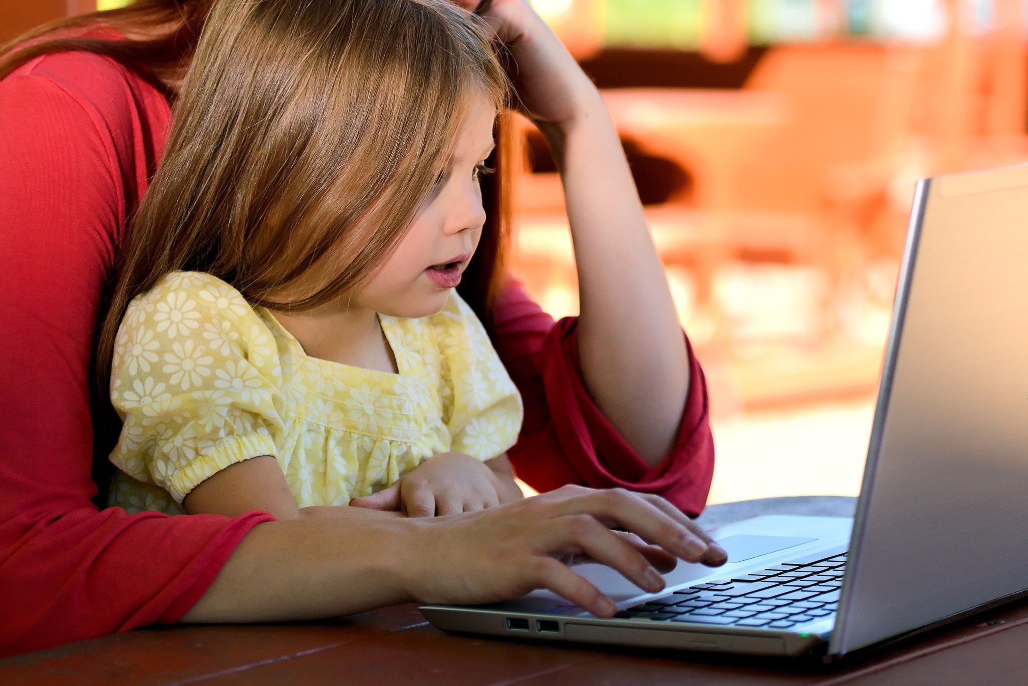 mother helping daughter on laptop
