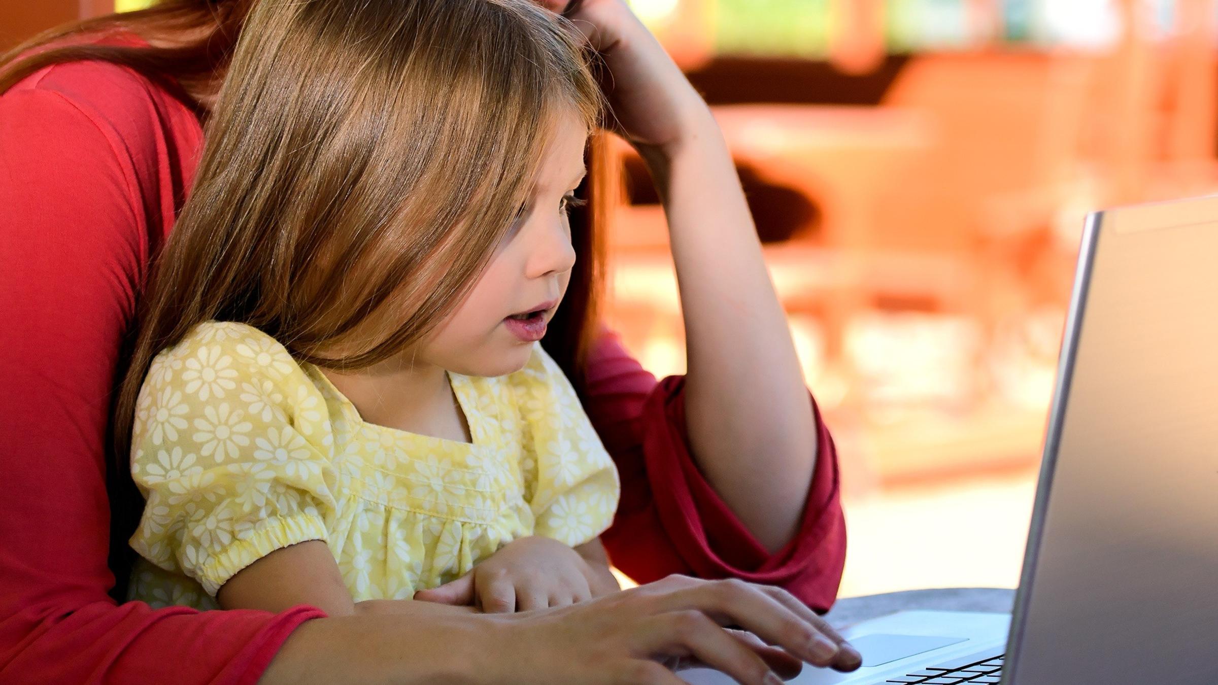 mother helping daughter on laptop