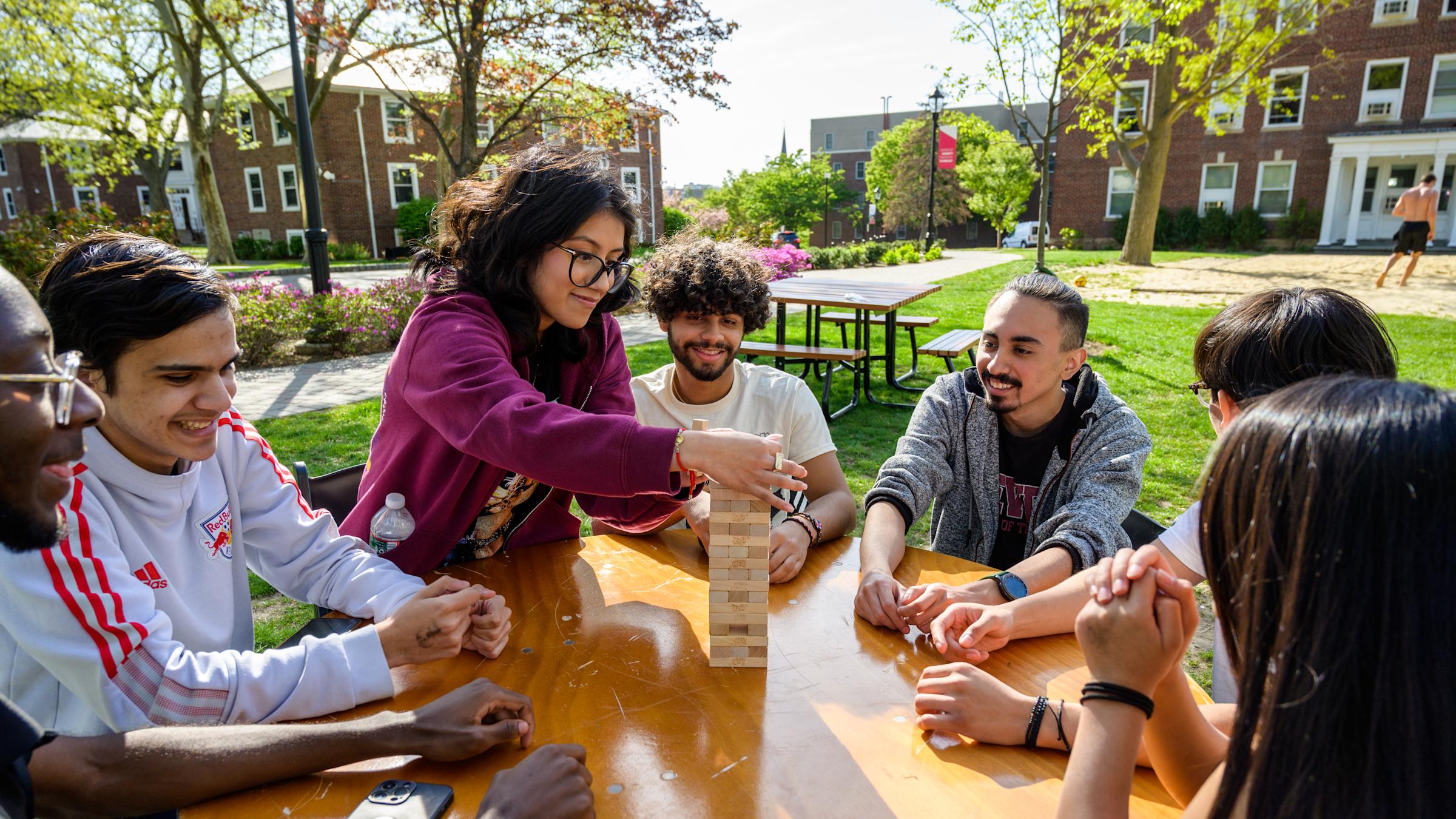Students gather outside to play Jenga on a table on campus