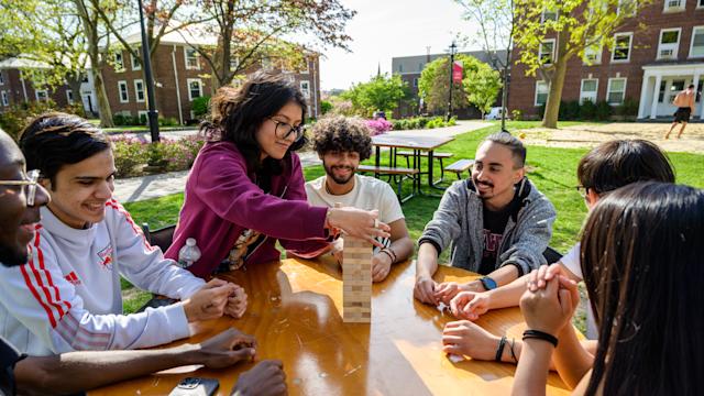 Students gather outside to play Jenga on a table on campus