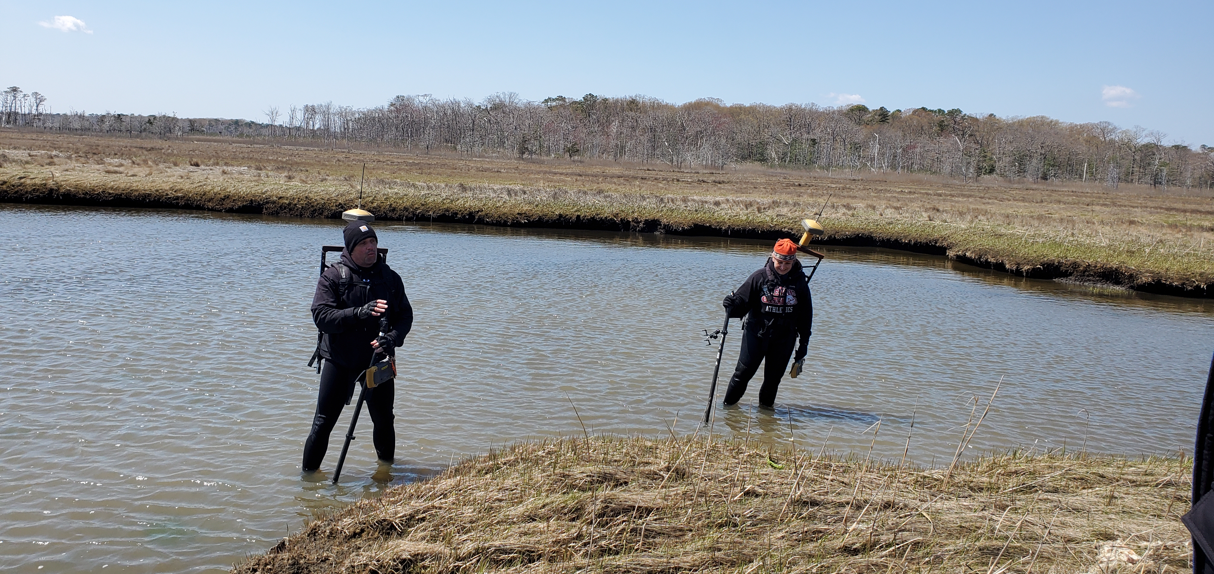 Jon Miller (left) and Laura Kerr standing in a shallow marsh with poles in the ground.