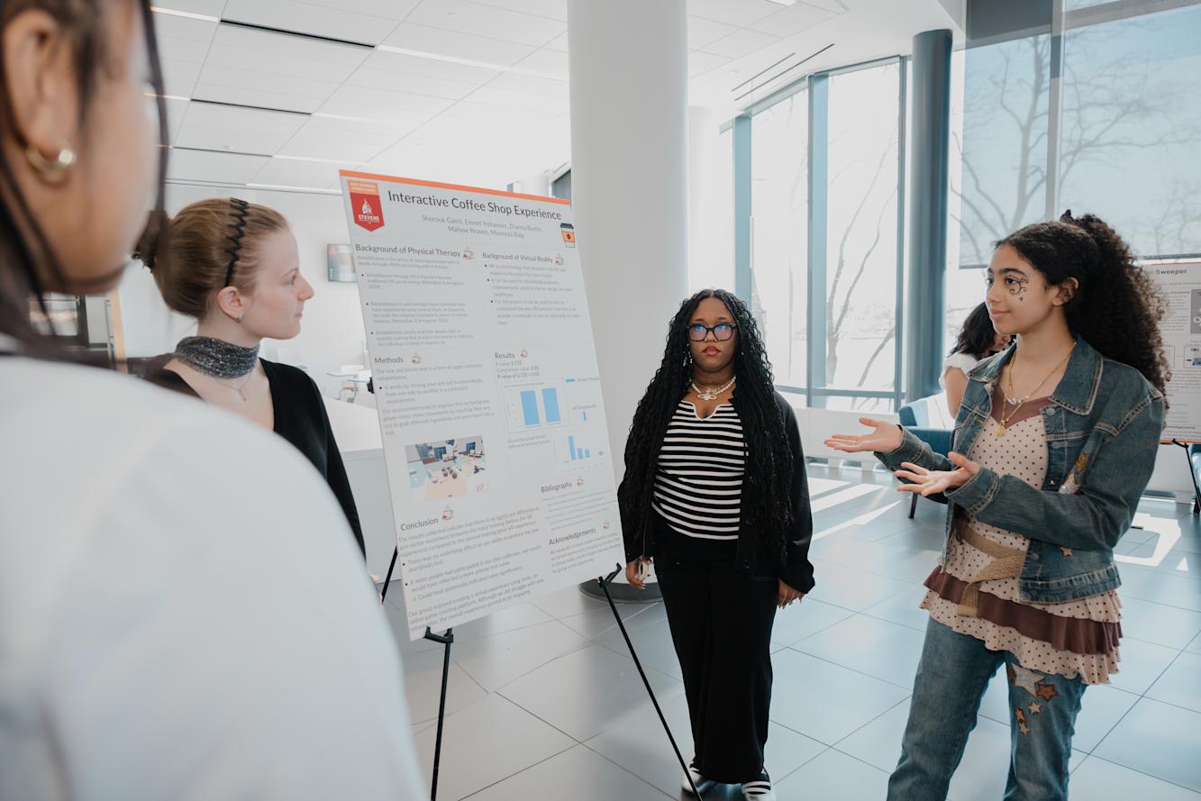 Two young women explain their poster to two other women.