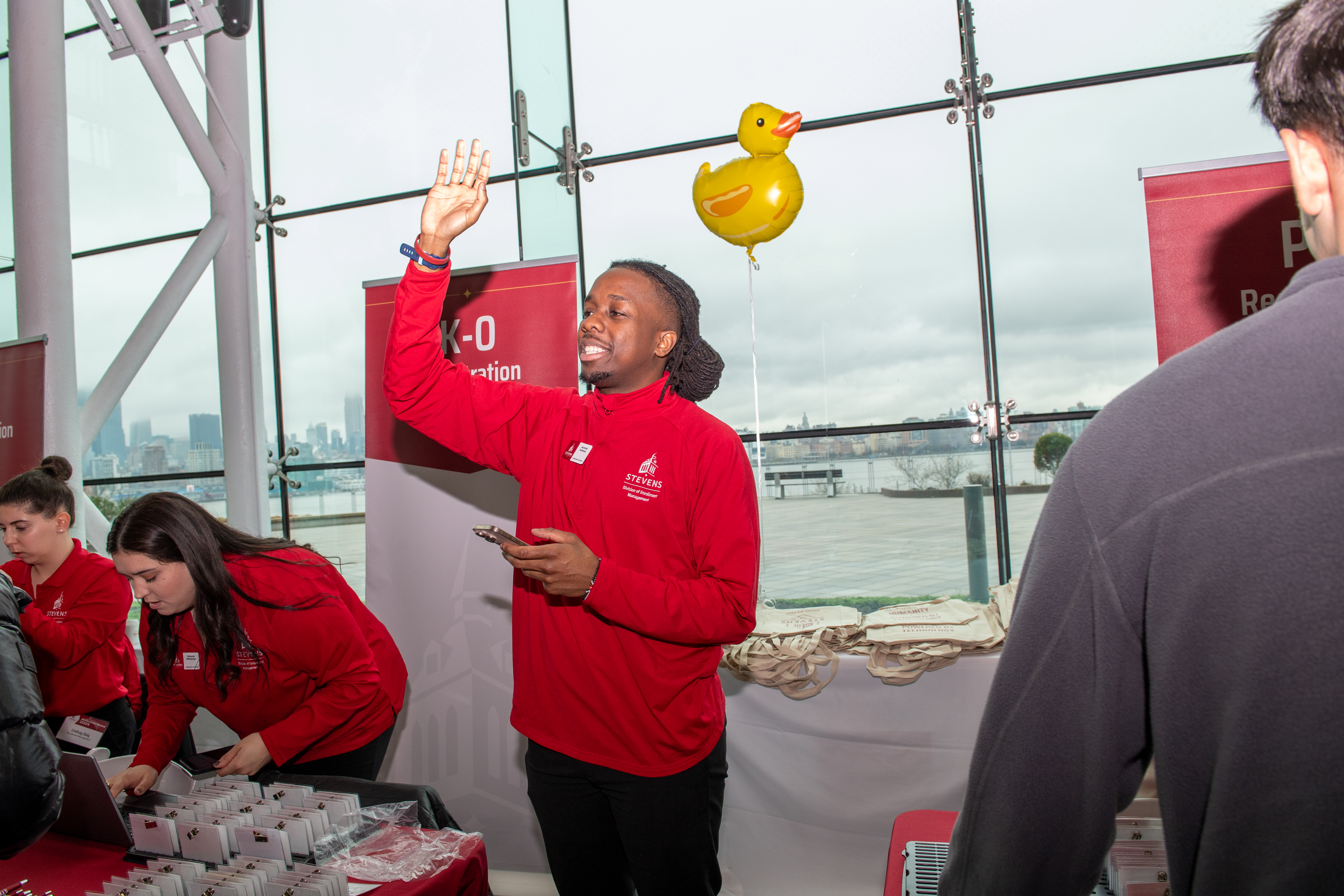 A man stands in front of duck balloon next to a table of name tags.