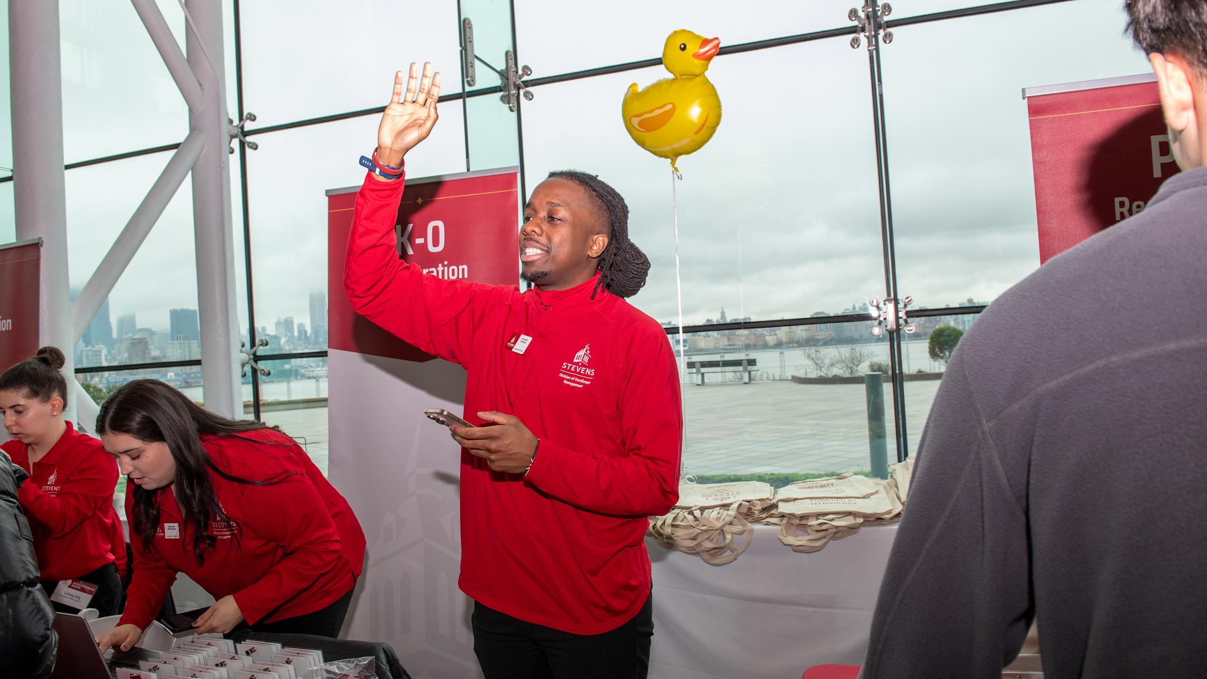 A man stands in front of duck balloon next to a table of name tags.