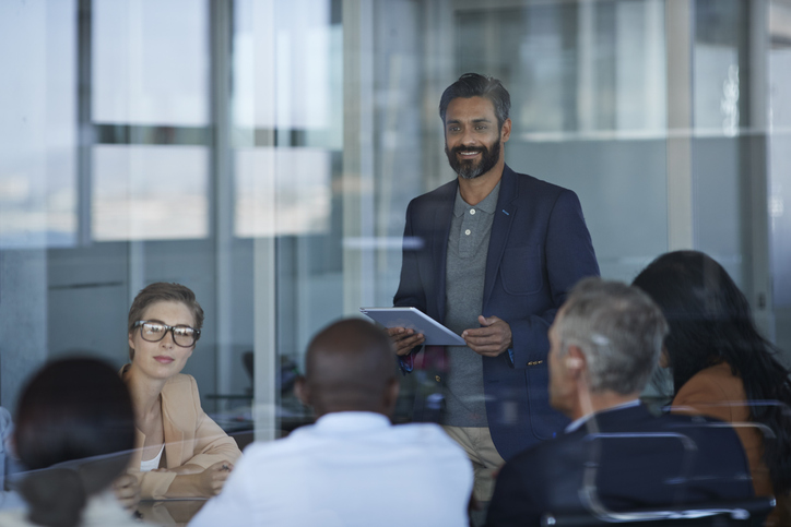 one man standing with sitting colleagues in conference room