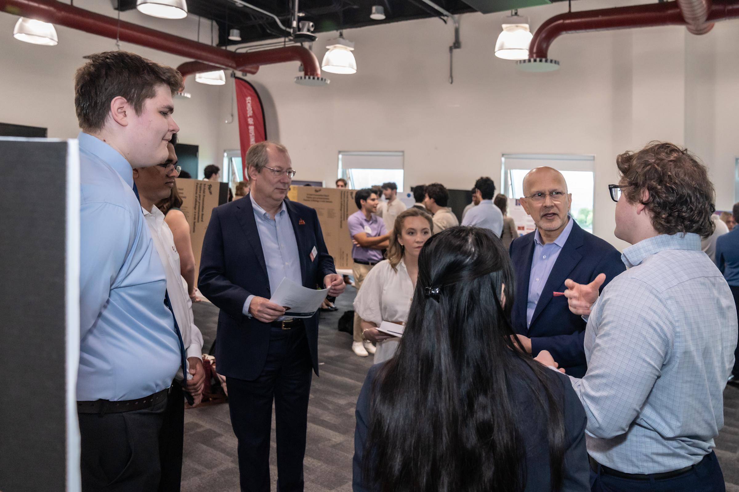 Three students present their project to a pair of visitors to their table.