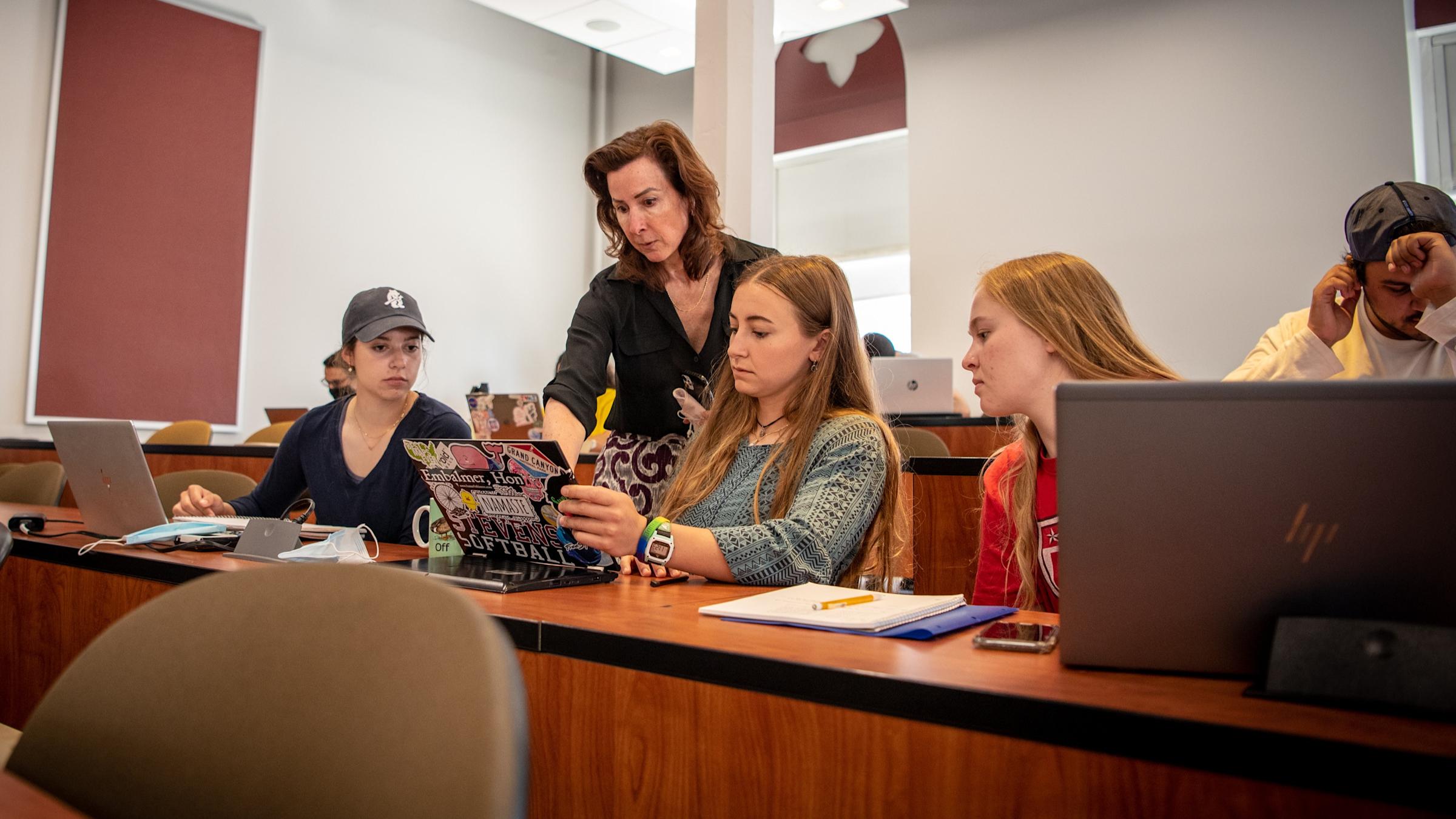 Three female students and a male student in a classroom with their female professor