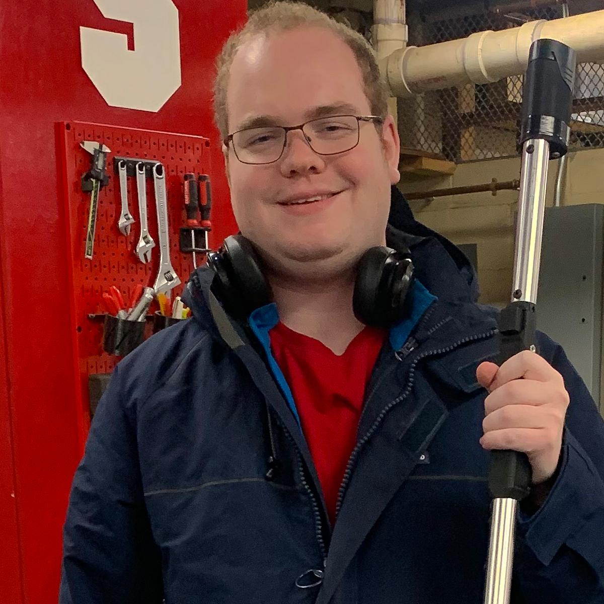 A young male standing in a workshop, smiling for the camera.