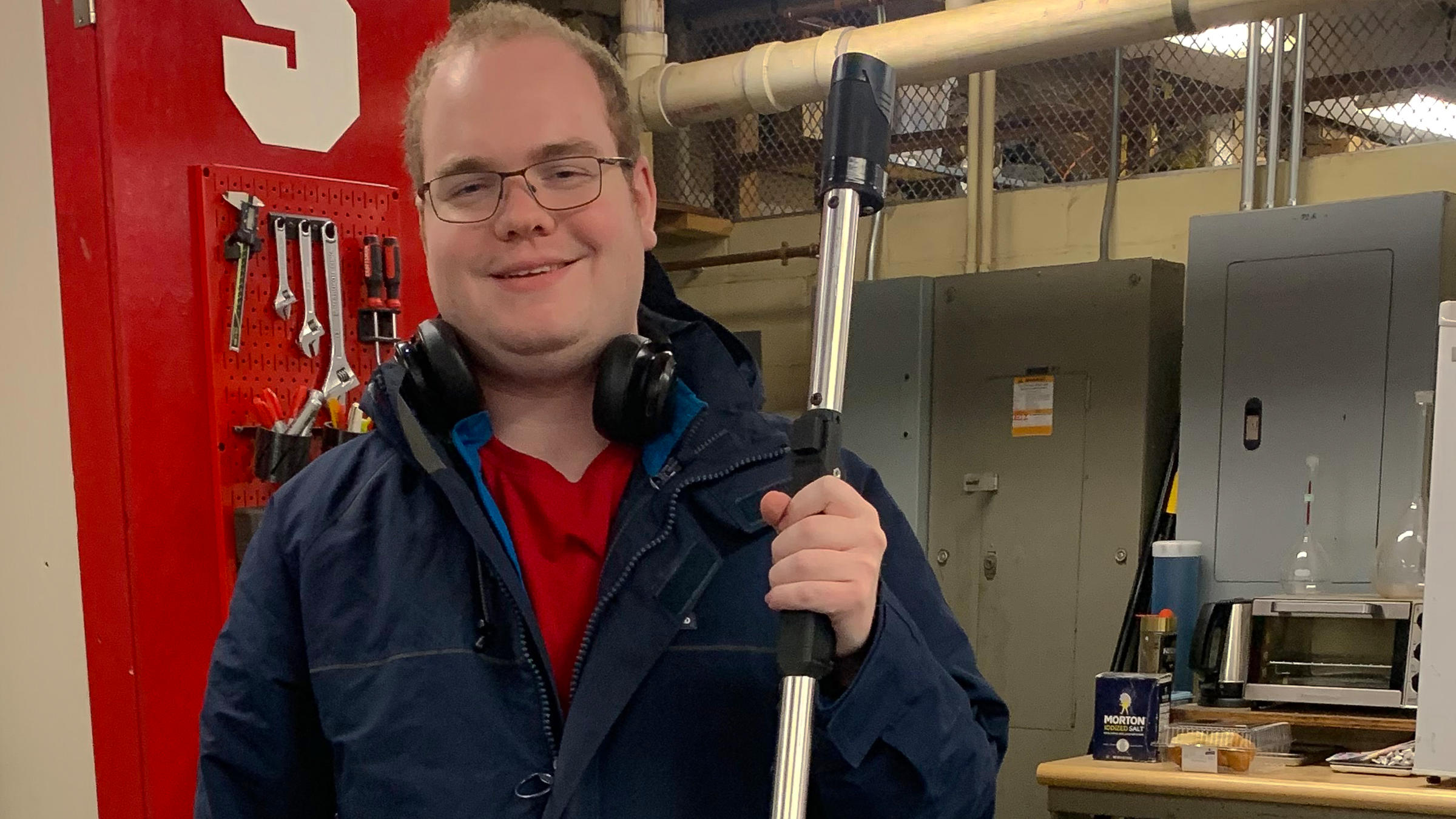 A young male standing in a workshop, smiling for the camera.