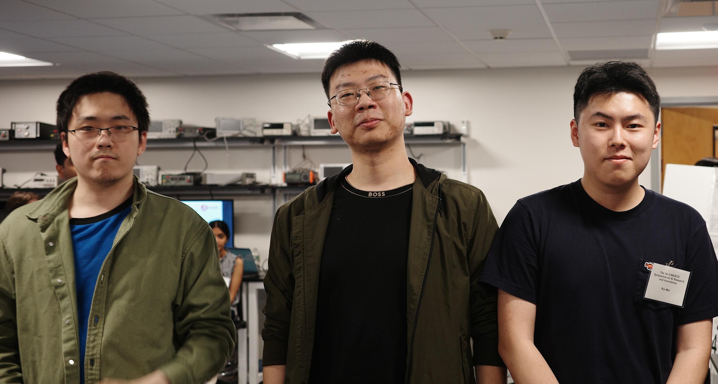 Three students stand next to each other in a lab looking at the camera.