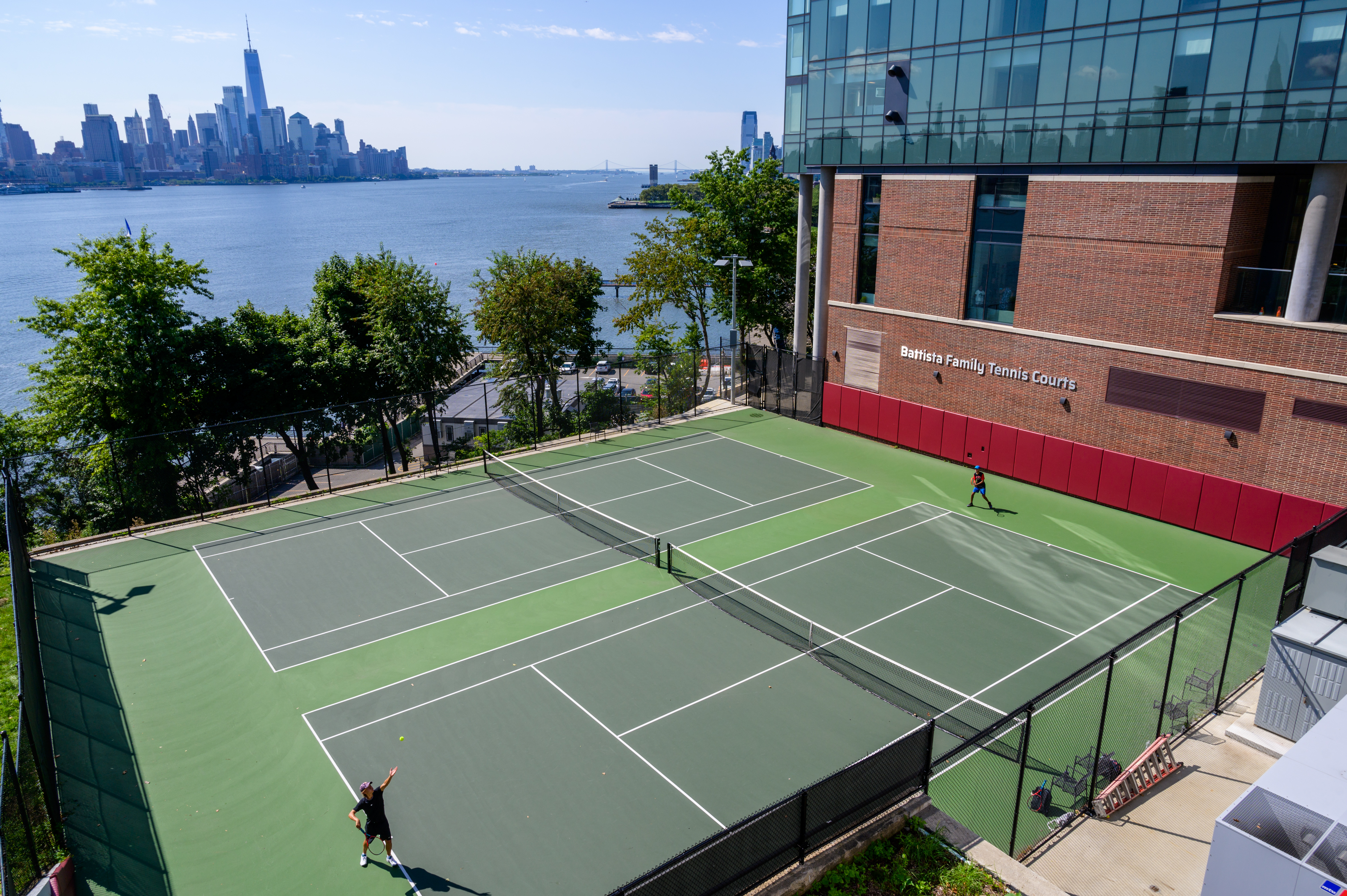 Students play on the Battista Family Tennis Courts with New York City skyline in the background