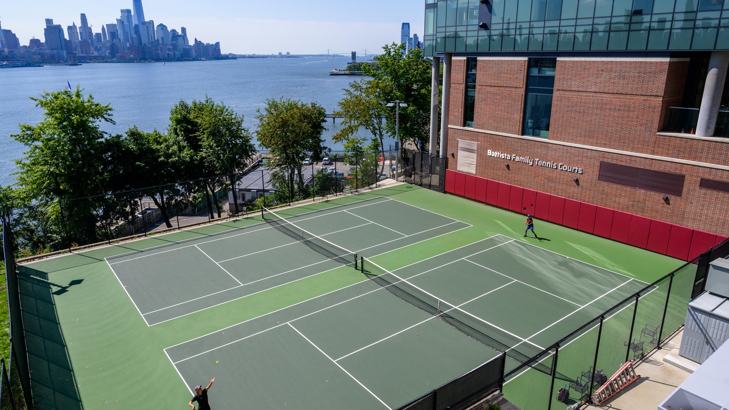 Students play on the Battista Family Tennis Courts with New York City skyline in the background