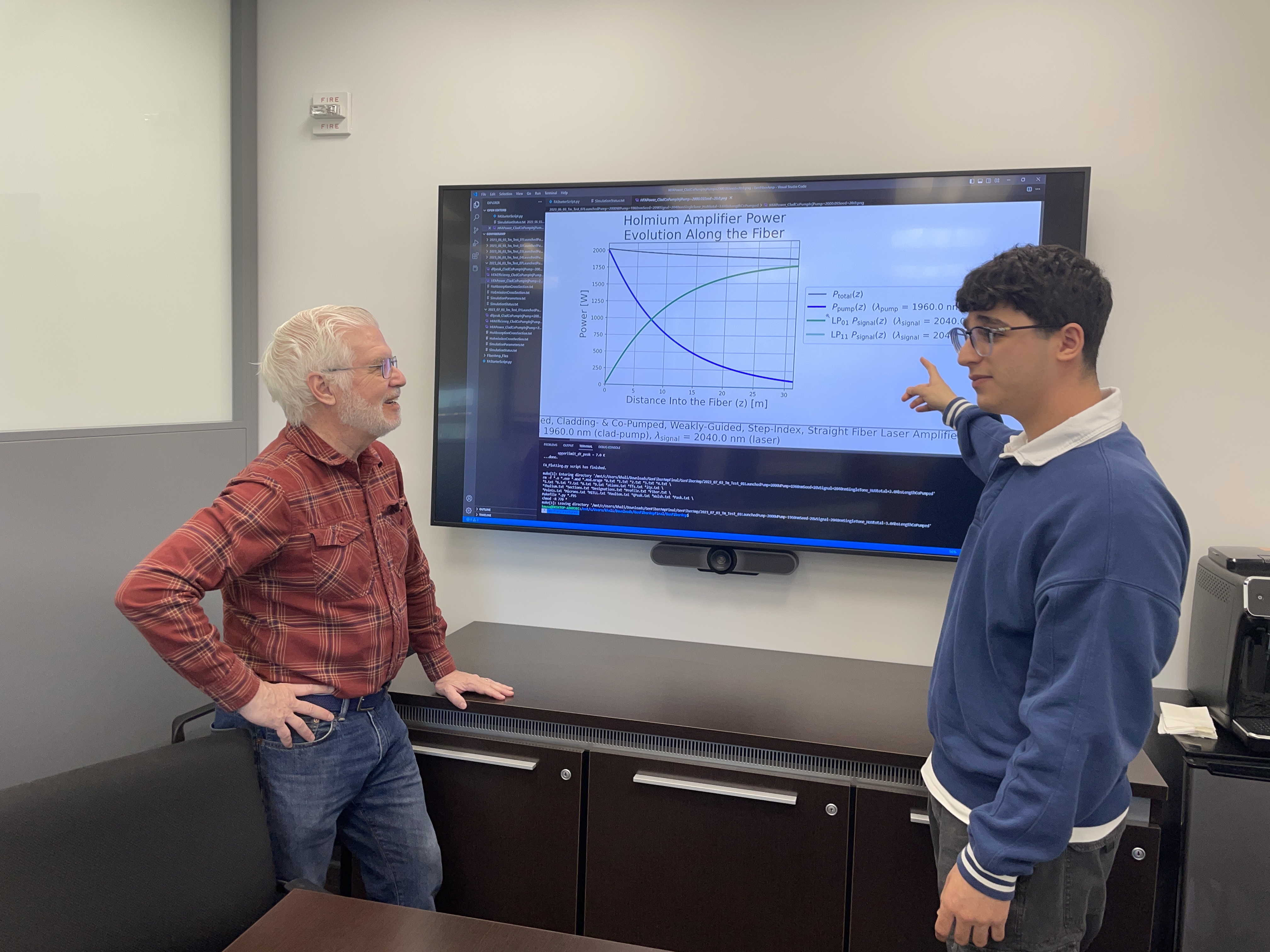 A photo of Ed Whittaker and Khalid Musa talking in front of a big screen with physics equations