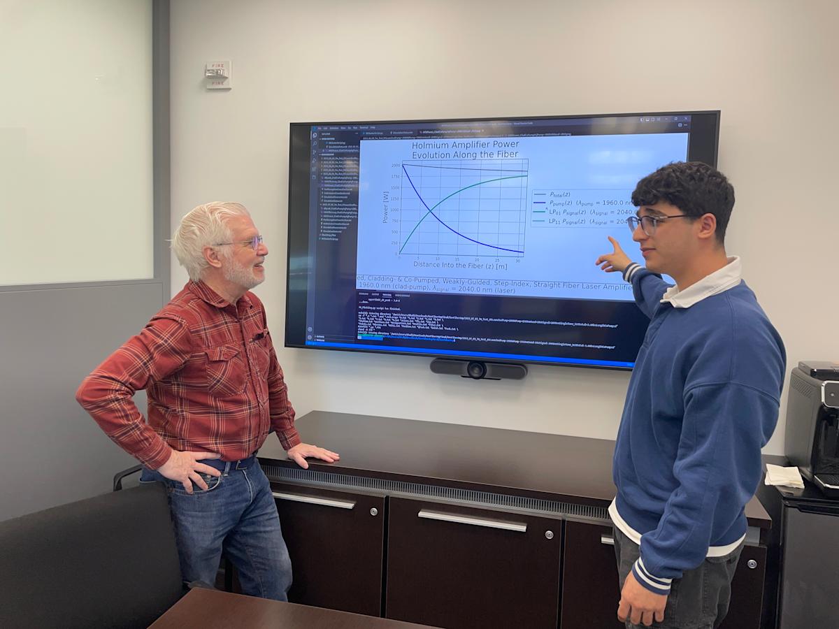 A photo of Ed Whittaker and Khalid Musa talking in front of a big screen with physics equations