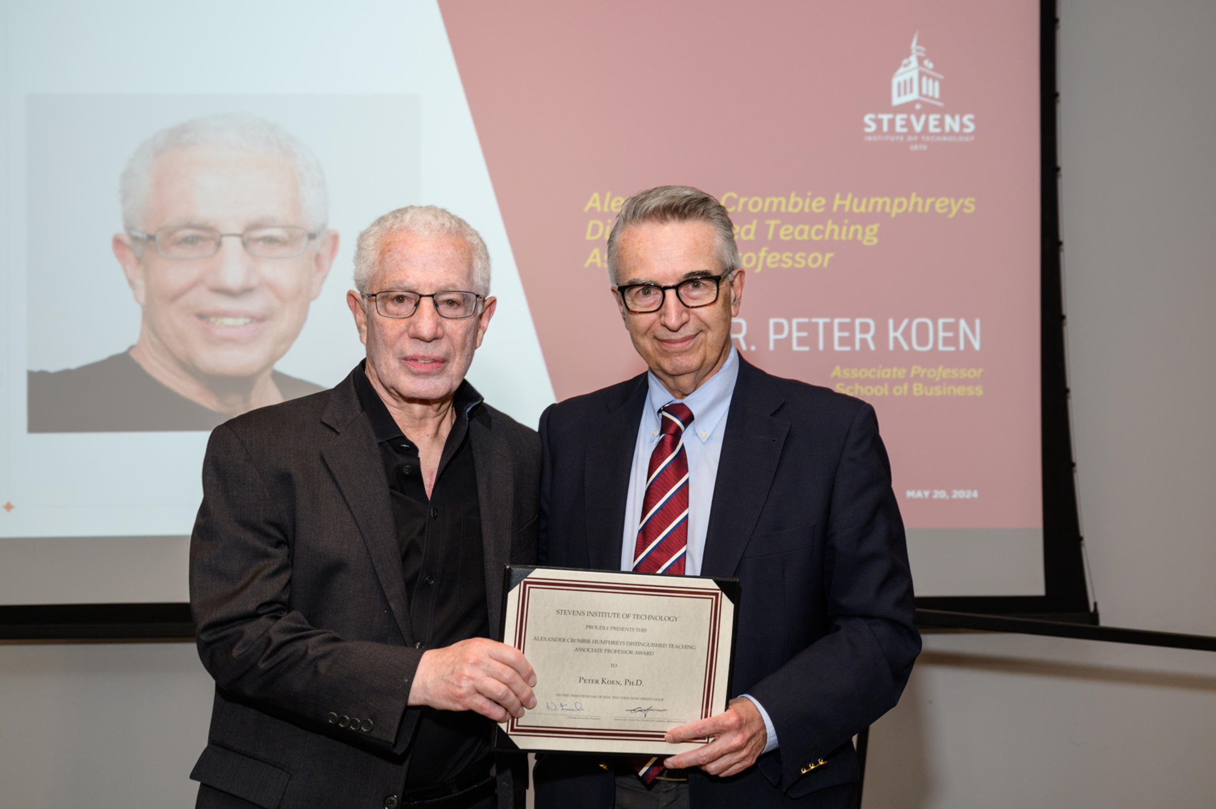 Peter Koen and Gregory Prastacos stand on the stage holding the award certificate.