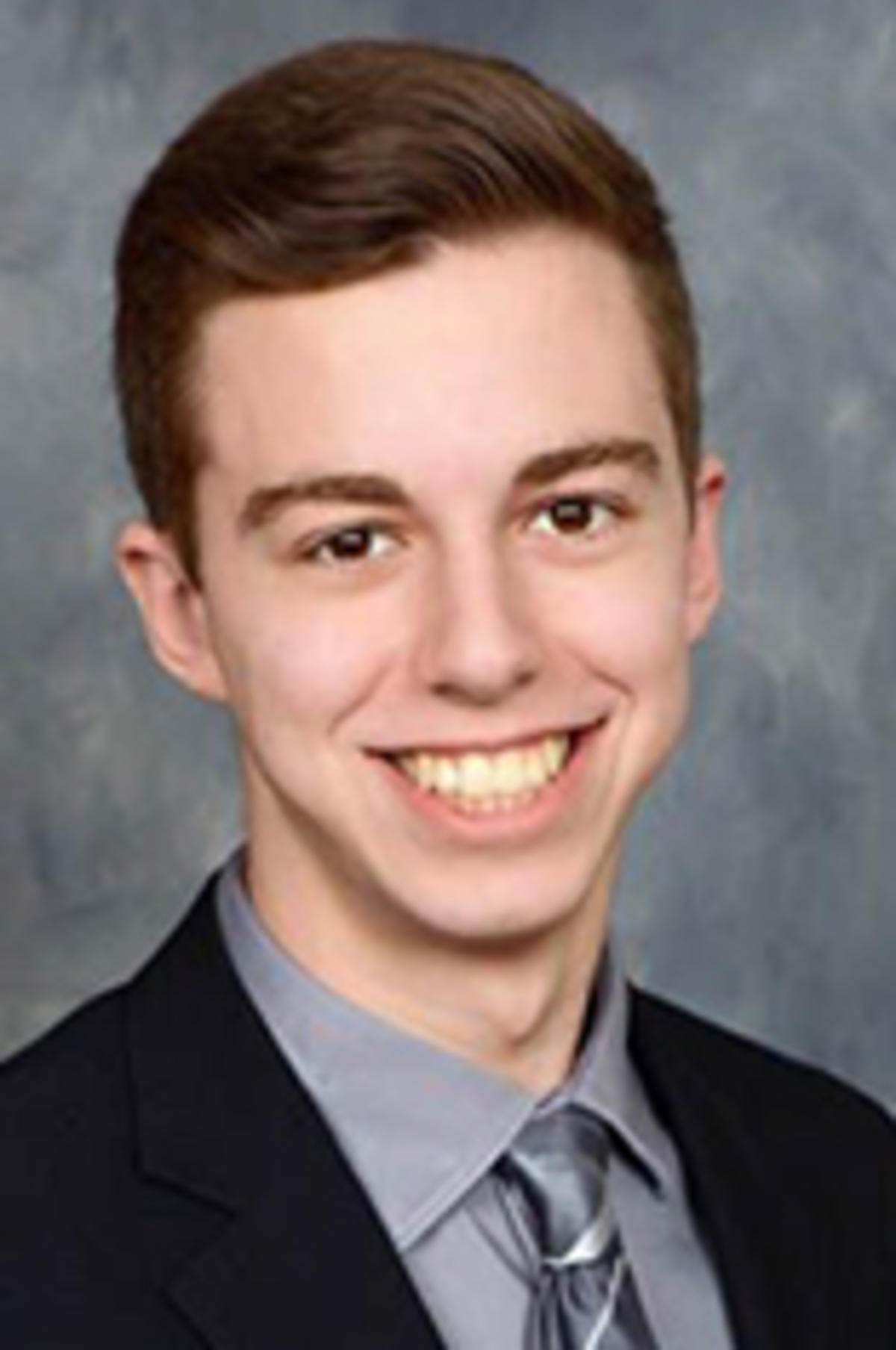 Headshot of Ryan Tom, in a dark suit against a gray background.