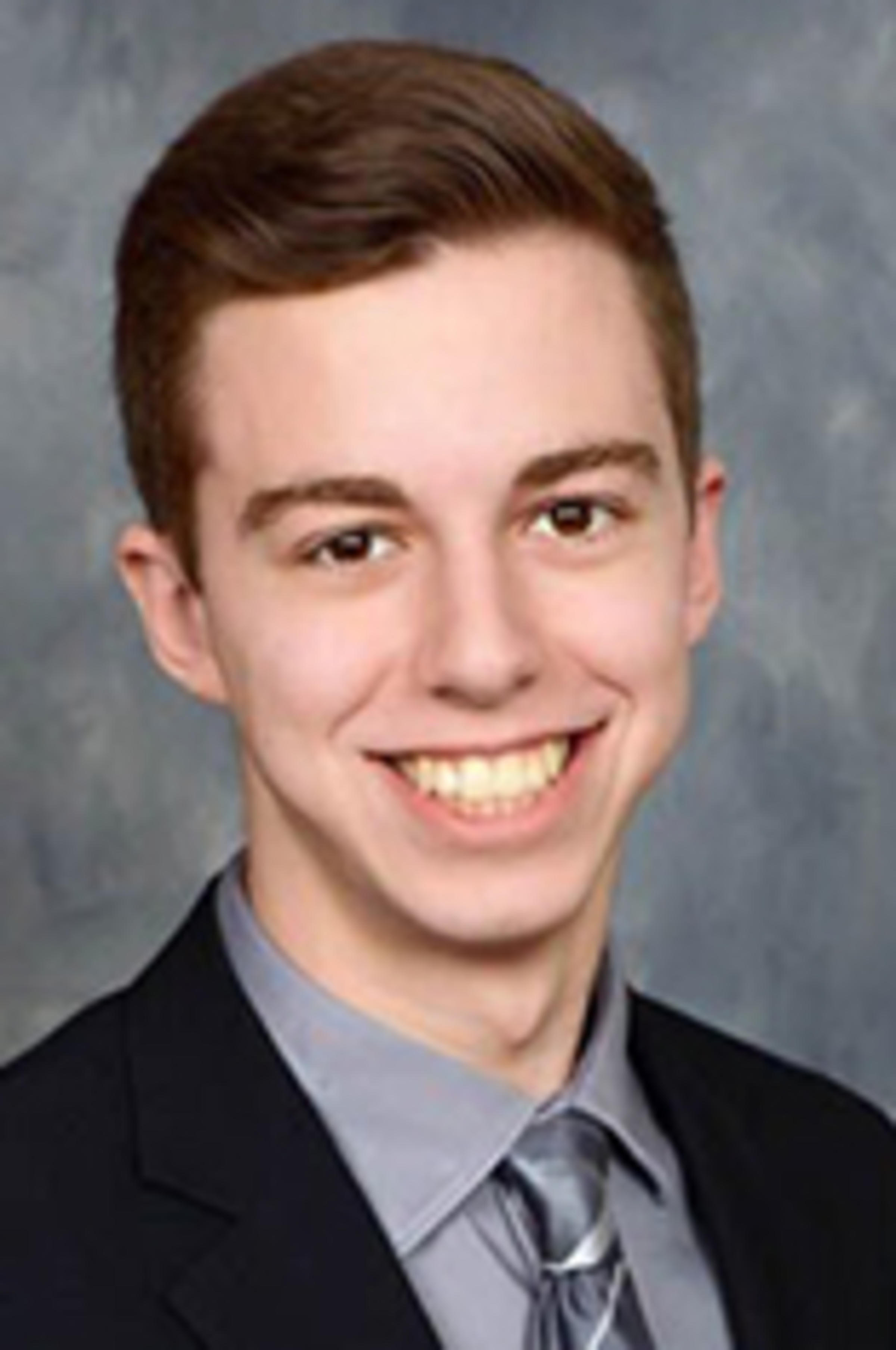 Headshot of Ryan Tom, in a dark suit against a gray background.