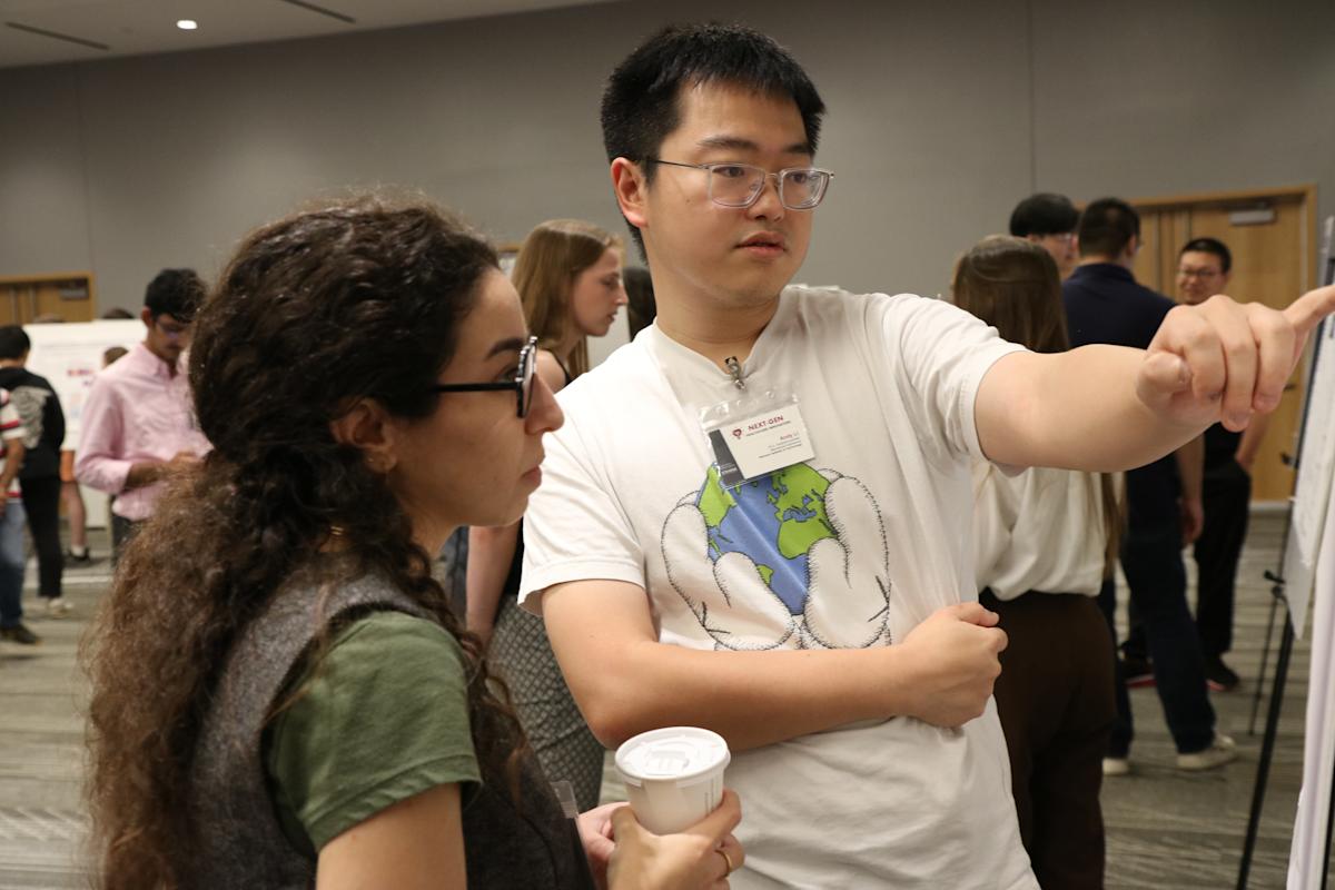 A female student on the left and a male student on the left photographed in the middle of a conversation about the research poster presentation in front of them.