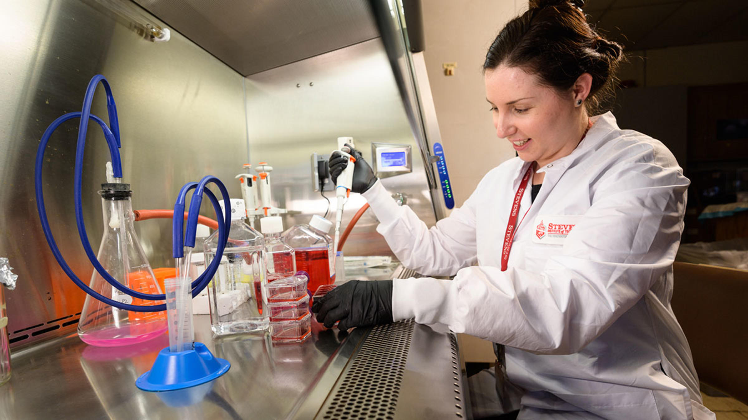 A female student in a lab coat works with chemistry equipment in a lab.