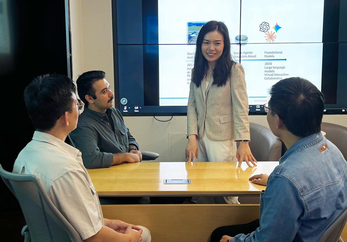 Ting Liao standing in front of three ph.d. students speaking with them about artificial intelligence models.