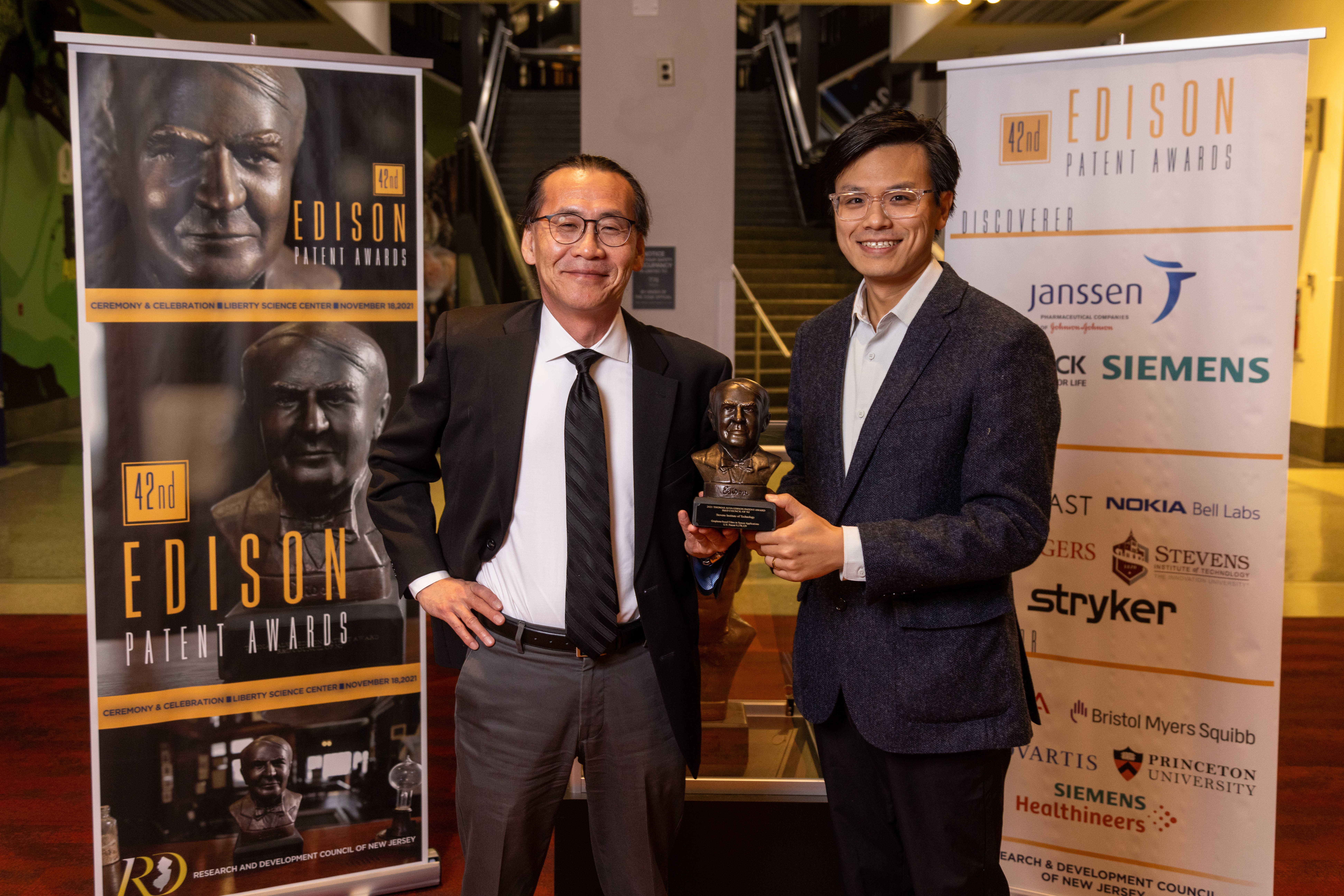 Two men, one holding a trophy, at Edison Patent Awards ceremony
