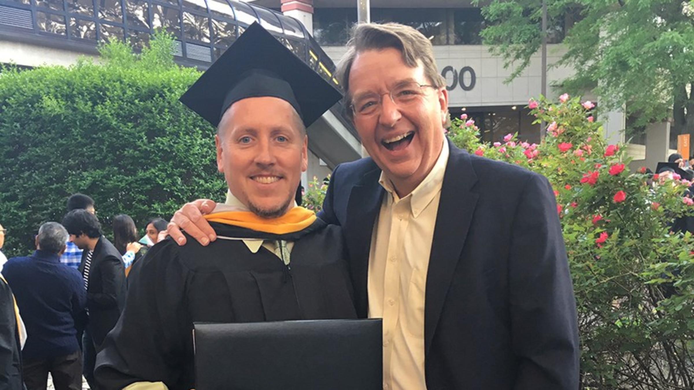 Kevin Storms, in graduation regalia, accepts congratulations from Kevin Ryan at commencement.