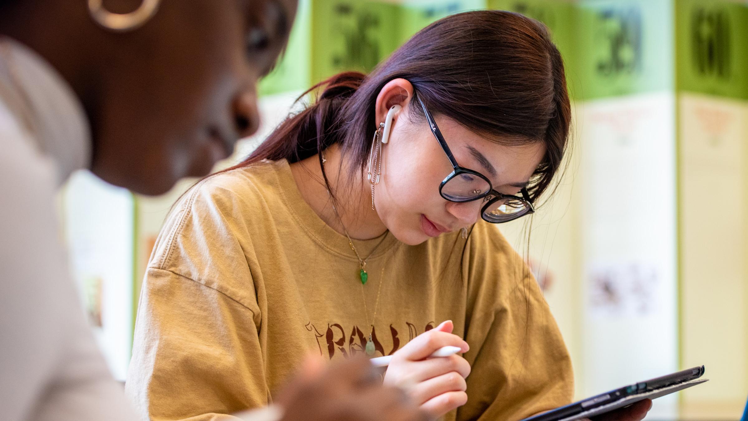 Students studying in library, with pen in hand.