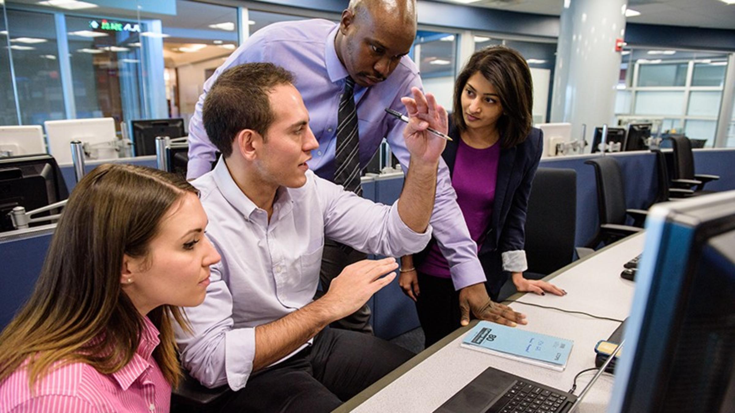 Four students working around a Bloomberg terminal in a high-tech finance lab.