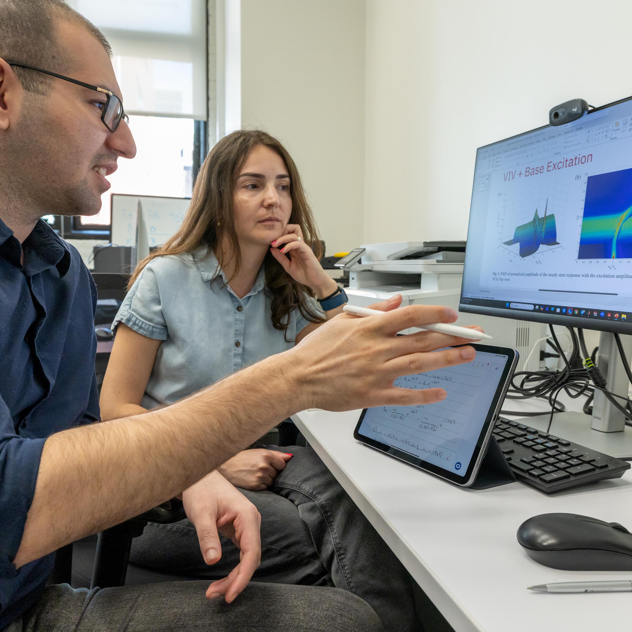 A student converses with the professor about information on a computer screen.
