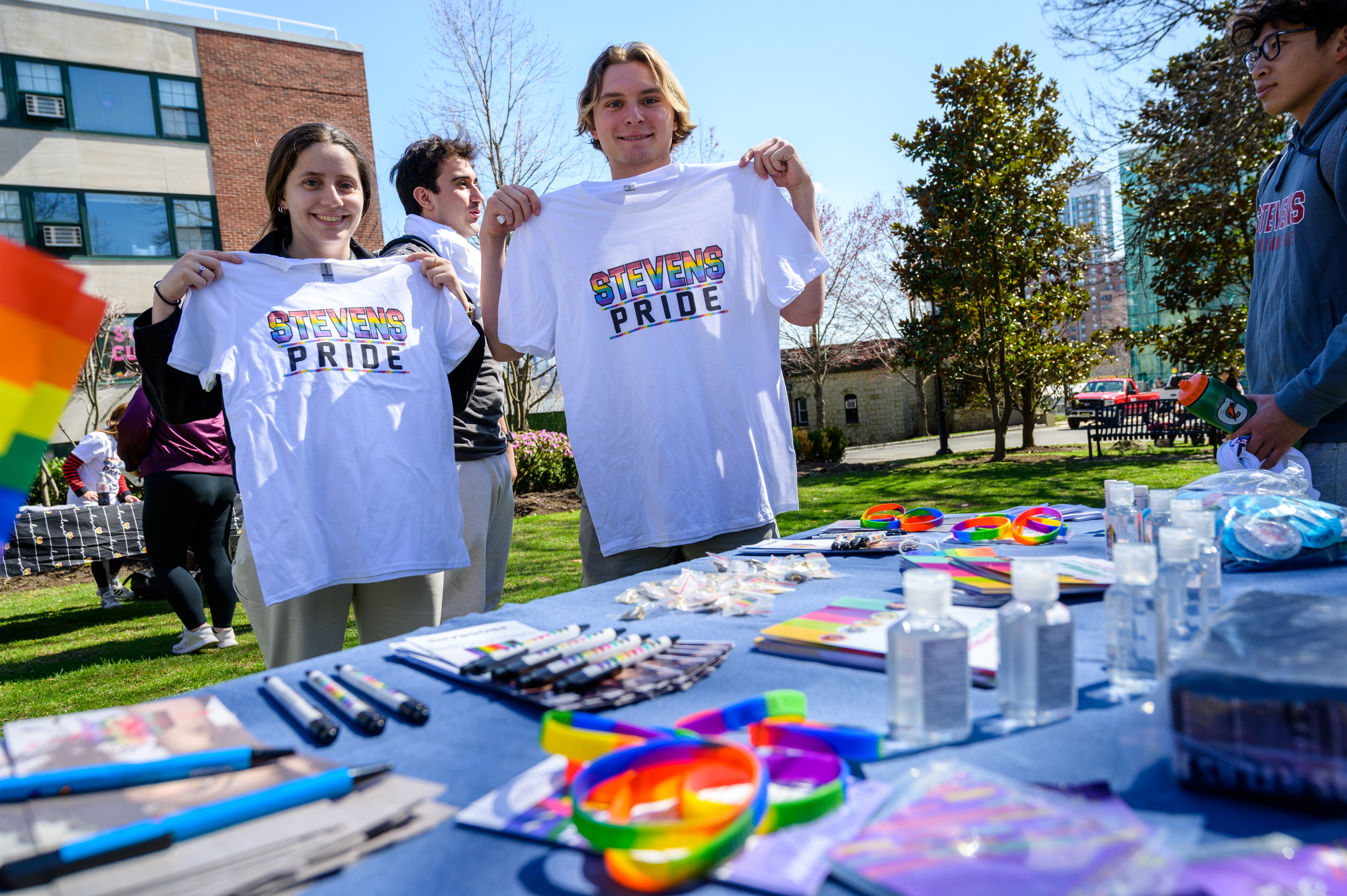 Photo of students holding up Stevens Pride t-shirts at a Pride themed table