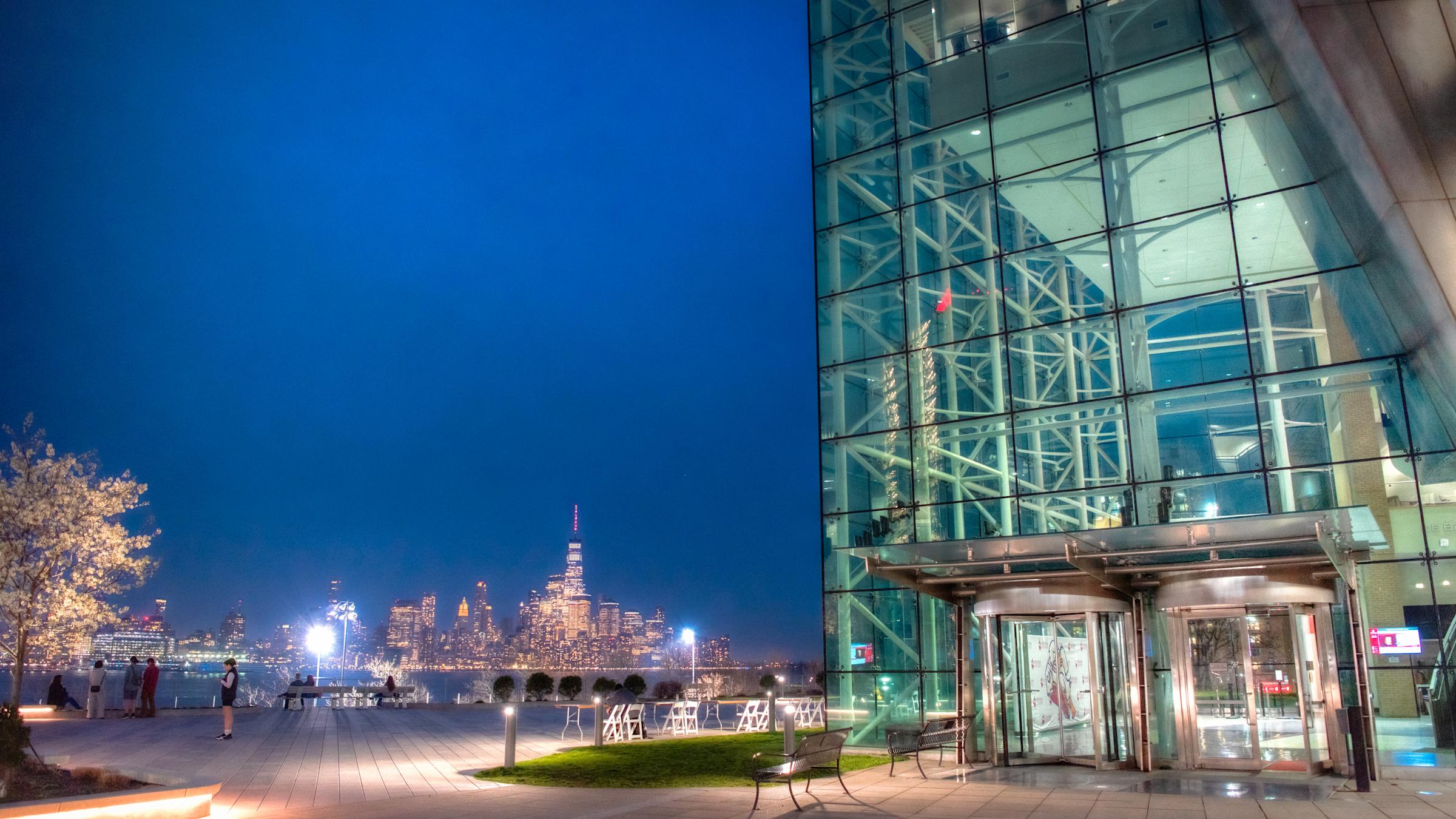 Babbio Center on Stevens campus lit up at night with New York City in background.