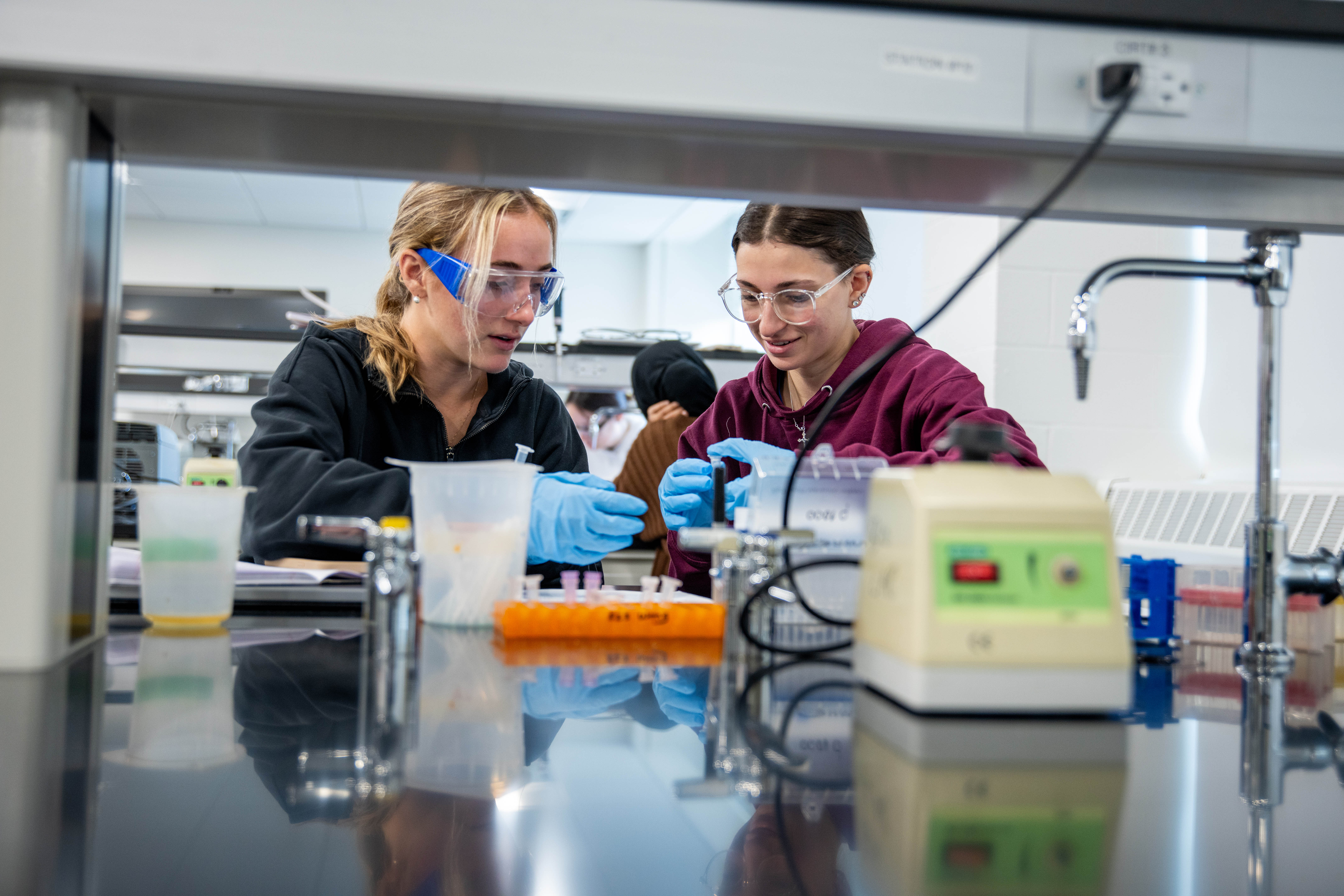 Two female students use medical equipment, including vials, in a lab setting.