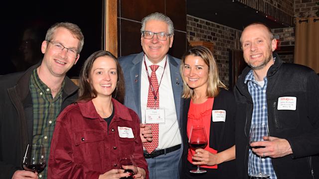 Five attendees pose for a photo at the Houston Alumni Holiday Gathering 2025, holding wine glasses in a warmly lit venue with brick walls.
